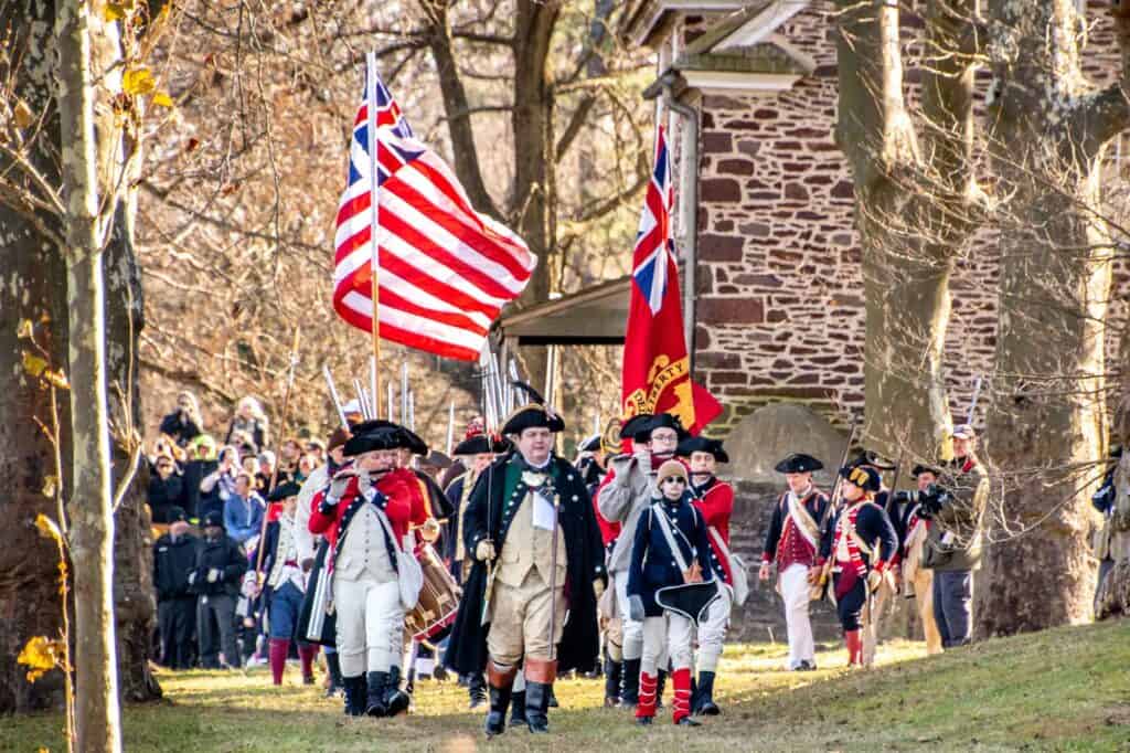 Pipers playing flutes and Revolutionary troops marching while carrying flags at the Washington Crossing reenactment