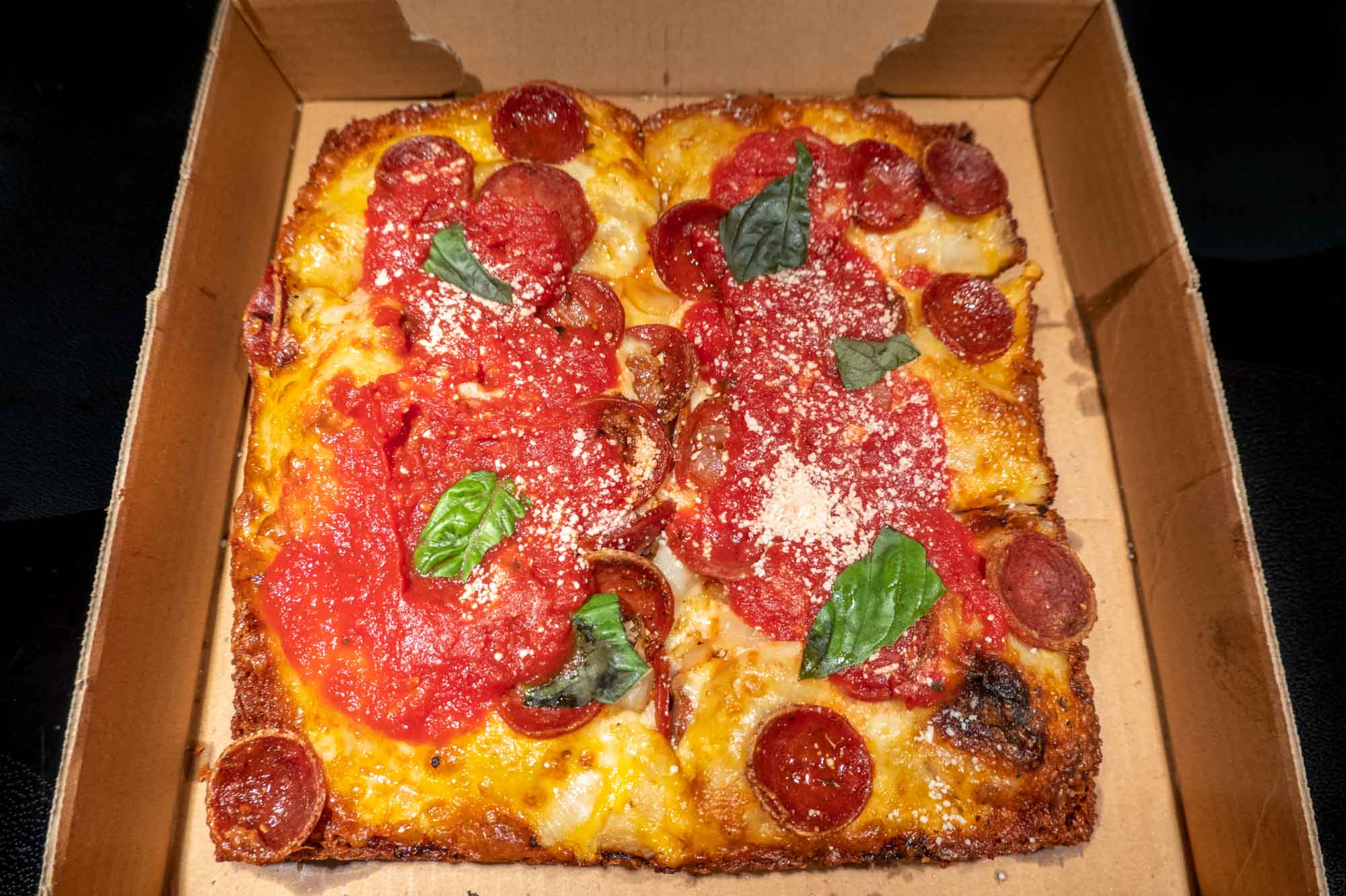 Square pizza topped with basil and pepperoni, and tomato sauce.