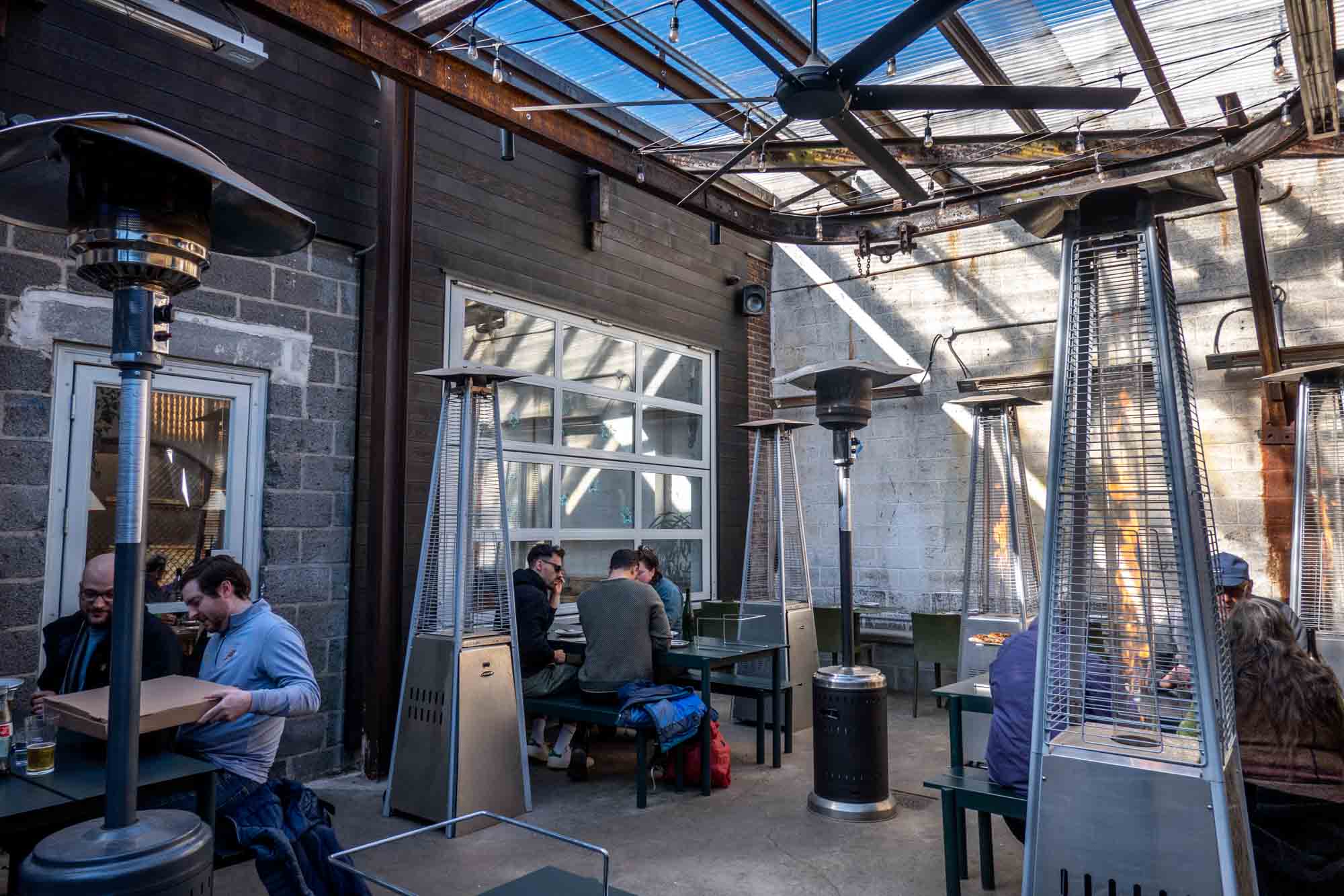 People sitting at outdoor tables at Pizzeria Beddia with heat lamps