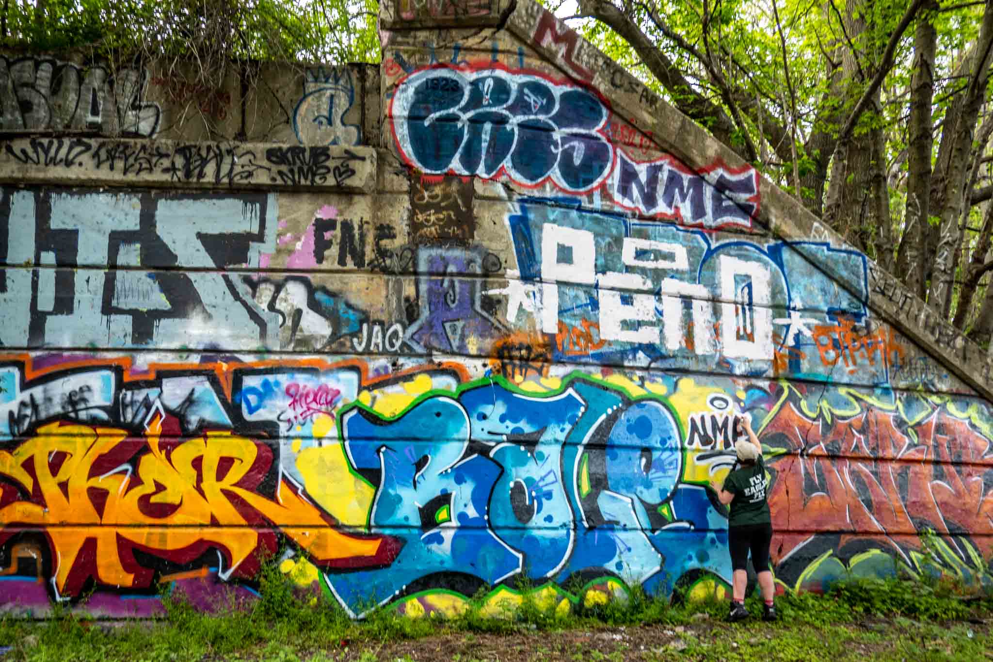 Person spray painting a wall full of bright graffiti.