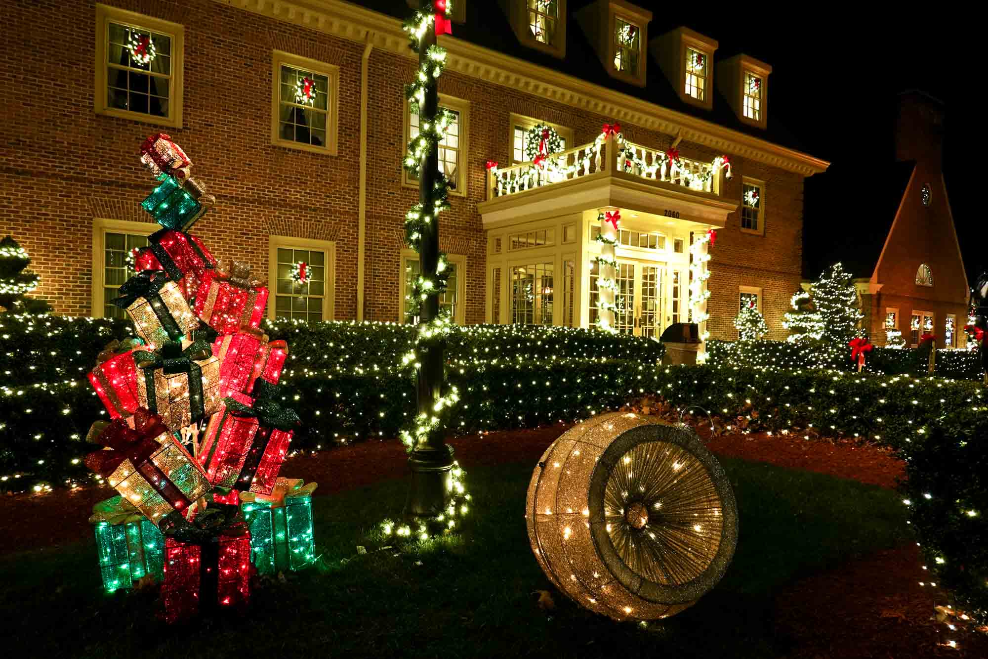 Illuminated ornaments and presents in front of a larger outdoor Christmas light display.