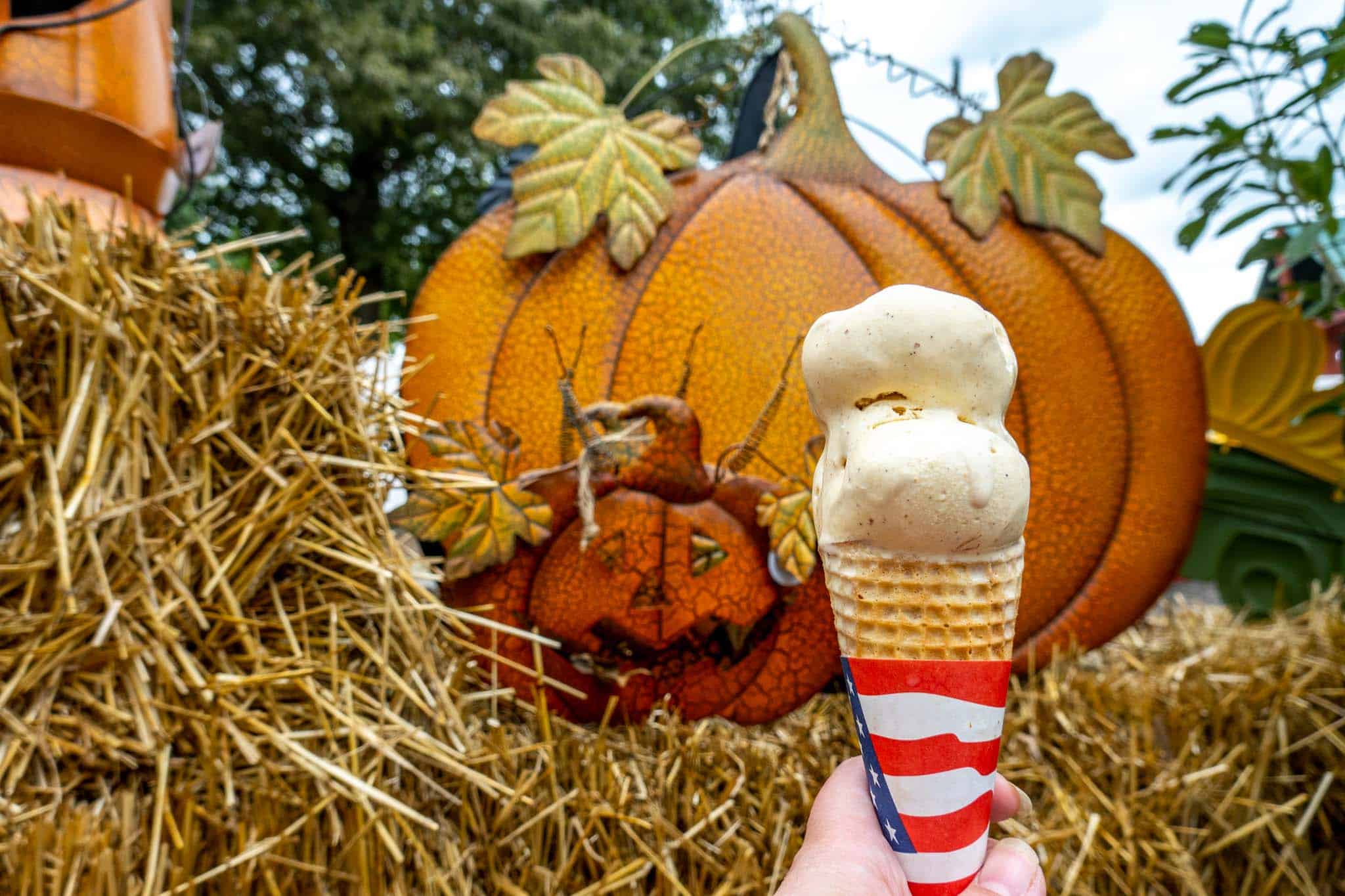 Ice cream cone held up in front of a metal pumpkin decoration sitting on a hay bale