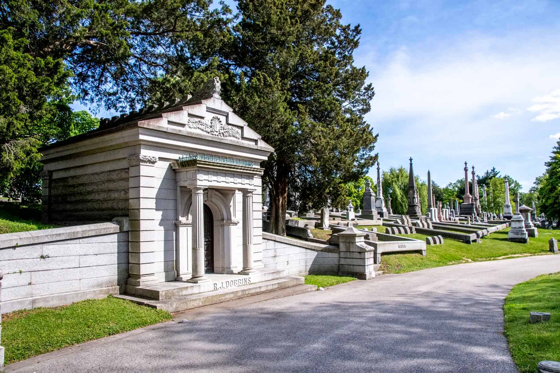 Gray mausoleum with columns next to a road in Laurel Hill Cemetery