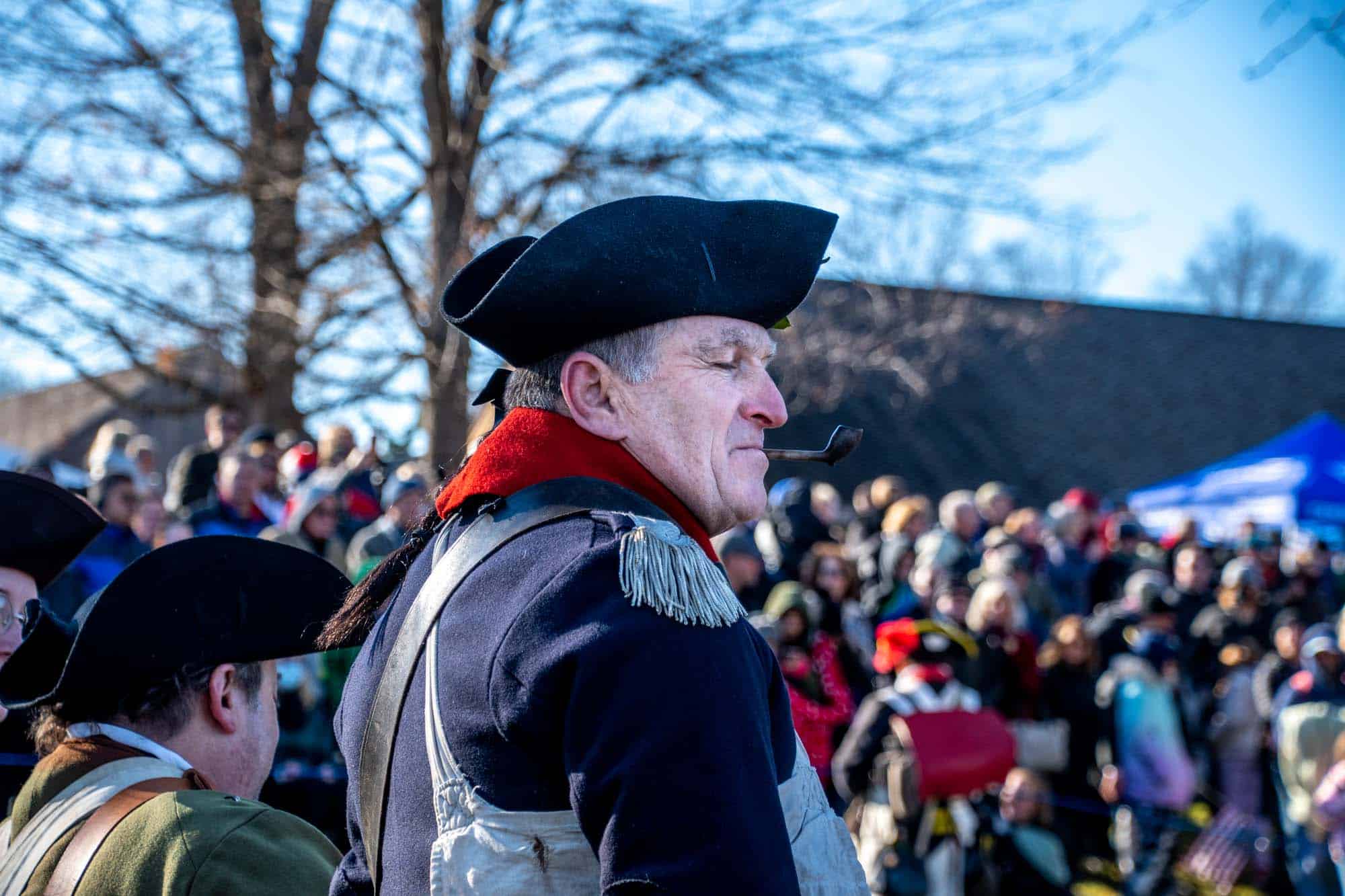 Reenactor smoking a pipe pauses in front of a crowd.