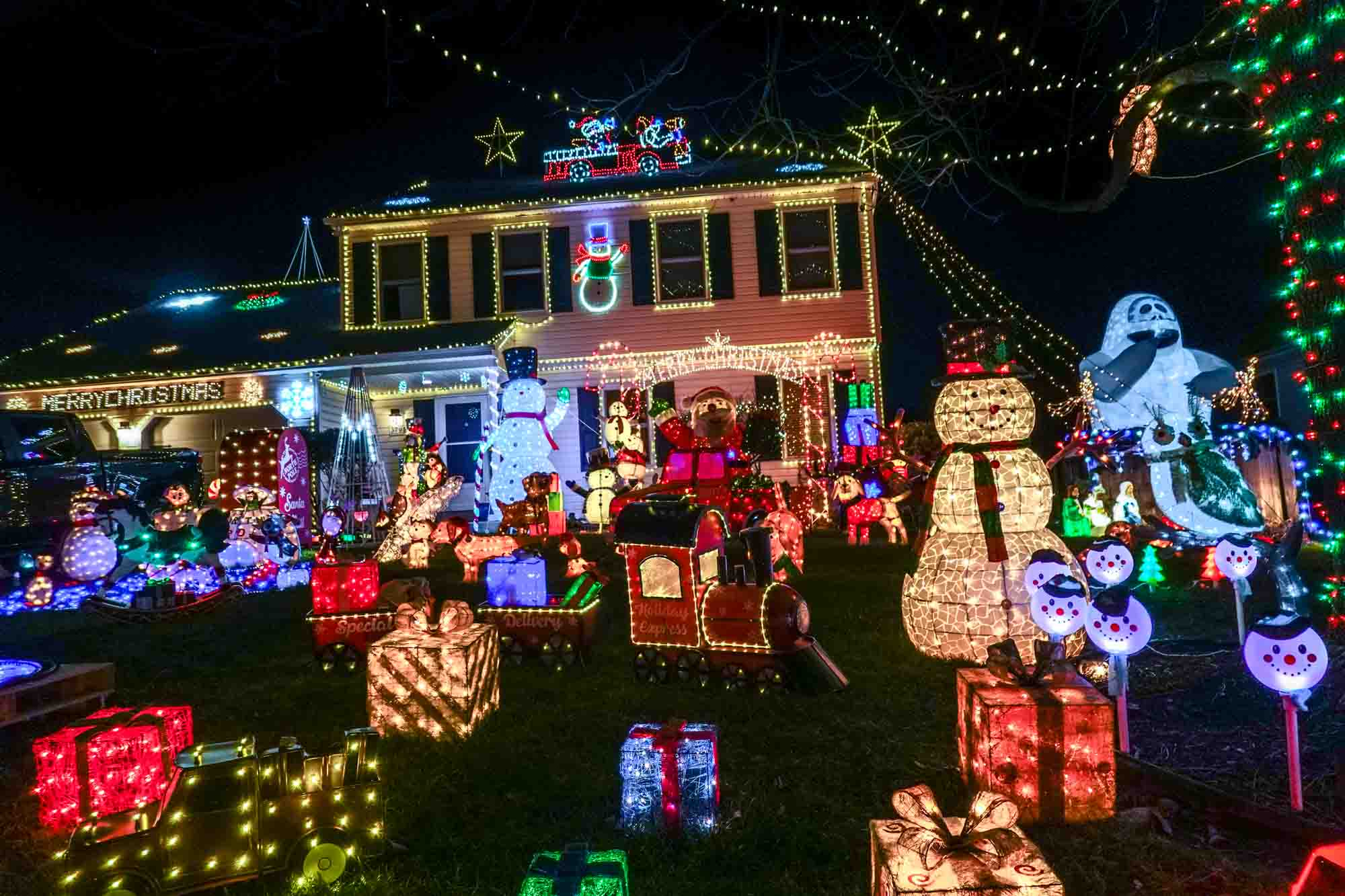 Illuminated presents, snowmen, and other decorations in a front yard.