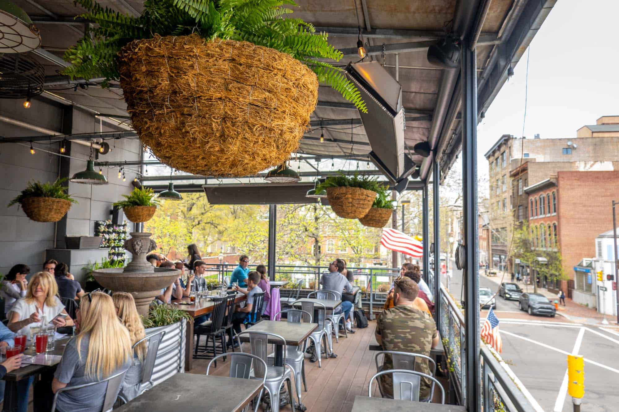 People sitting at a rooftop restaurant with hanging planters and a retractable roof.