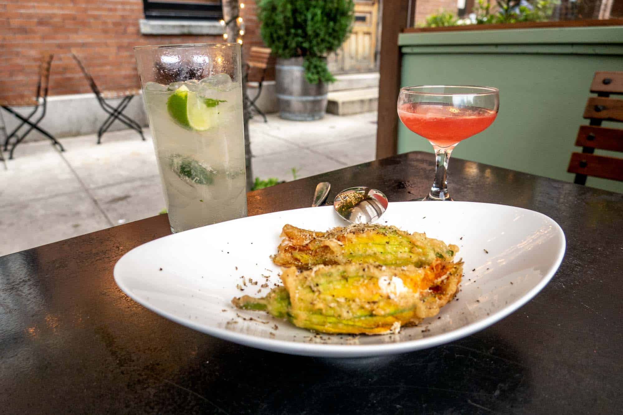 Fried zucchini blossoms on a plate beside two cocktails.