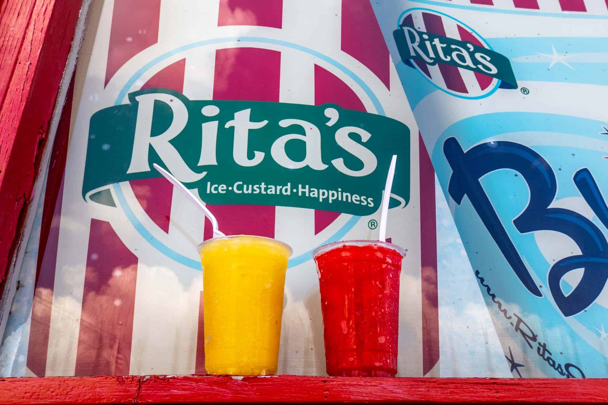 Two cups filled with yellow and red ice by sign: "Rita's, Ice, Custard, Happiness."