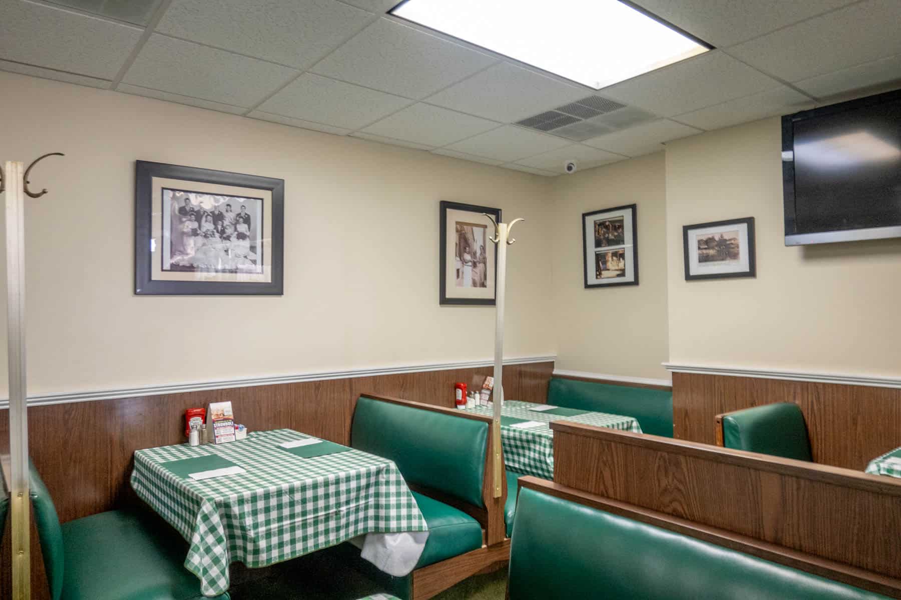 Booths in an Italian eatery with green and white tablecloths and family photos on the wall