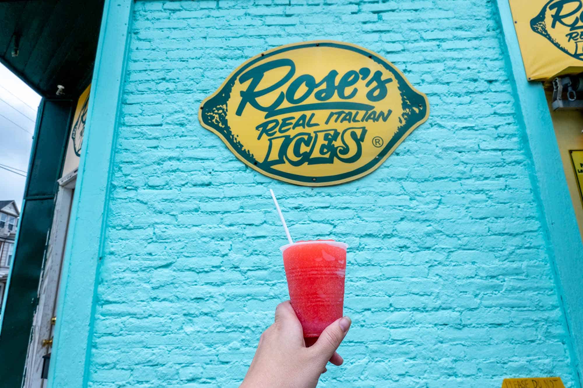 Cup filled with cherry ice in front of sign: "Rose's Real Italian Ices."