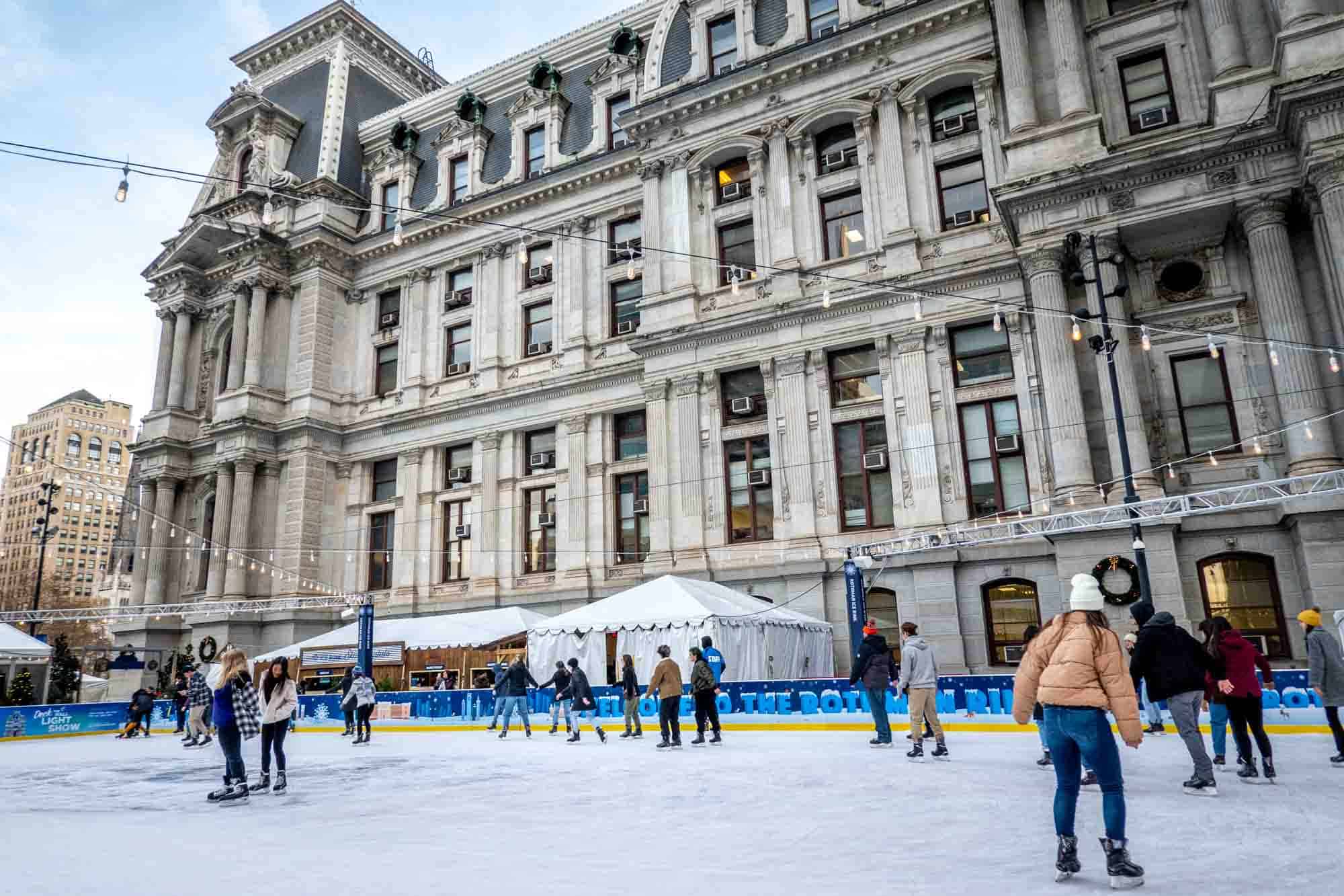 People skating on an ice-skating rink beside a large gray building