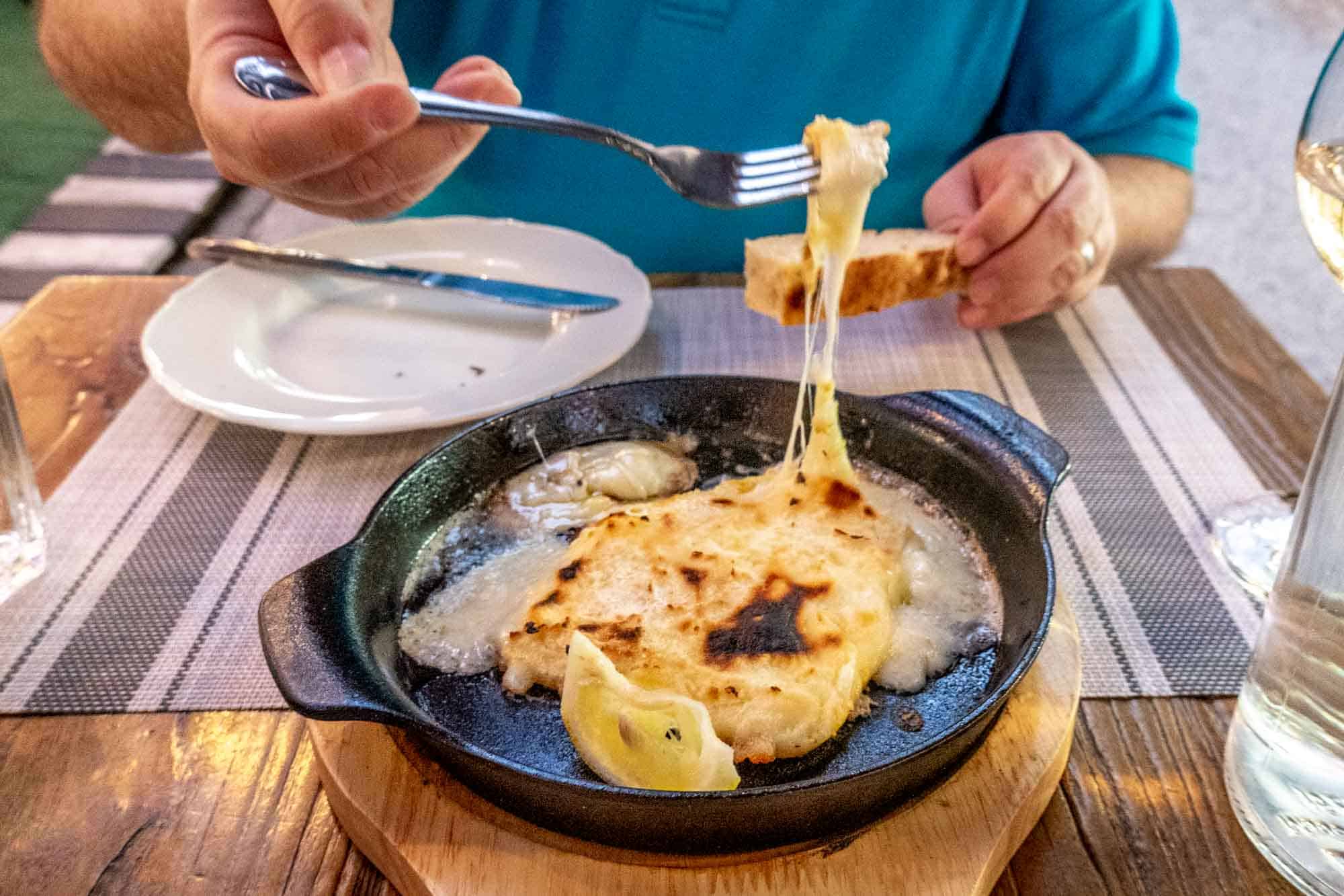Gooey saganaki cheese being pulled out of cast iron dish