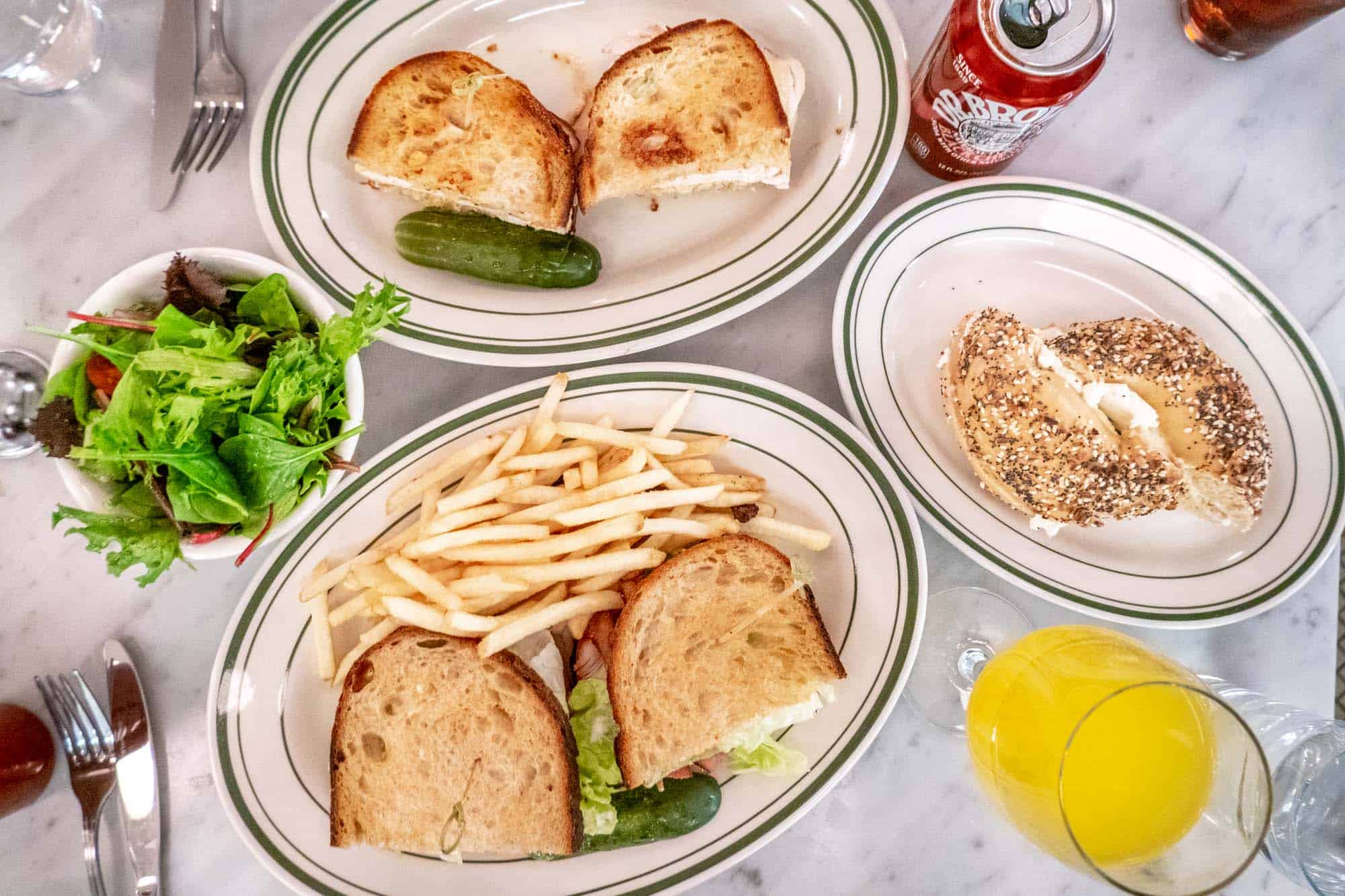 Sandwiches on a restaurant table with a salad, French fries, and a bagel
