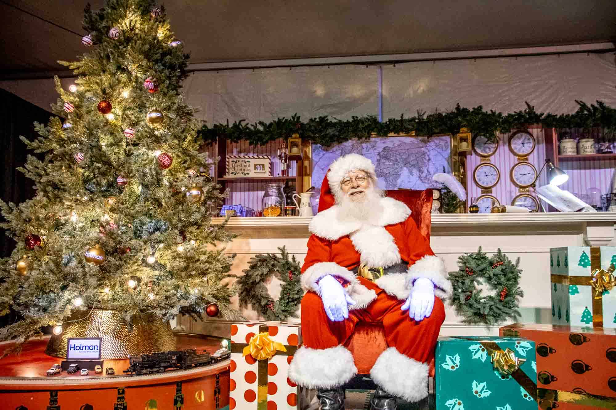 Santa sitting among presents and a Christmas tree.
