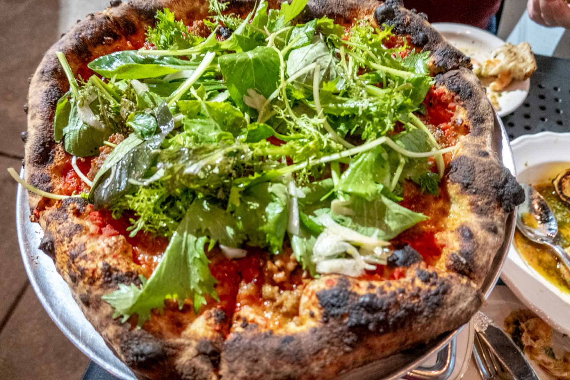 Sausage pizza topped with salad on a metal serving tray