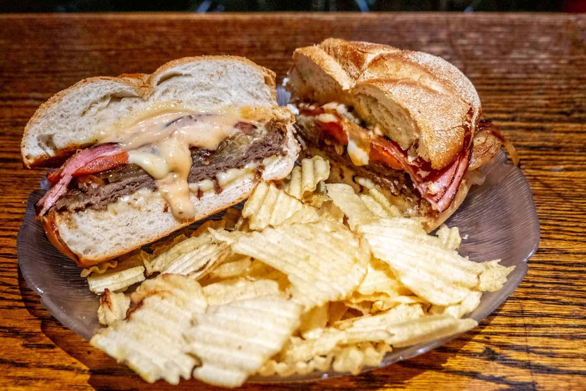 Sandwich with roast beef and orange sauce on a round roll on a plate with potato chips.