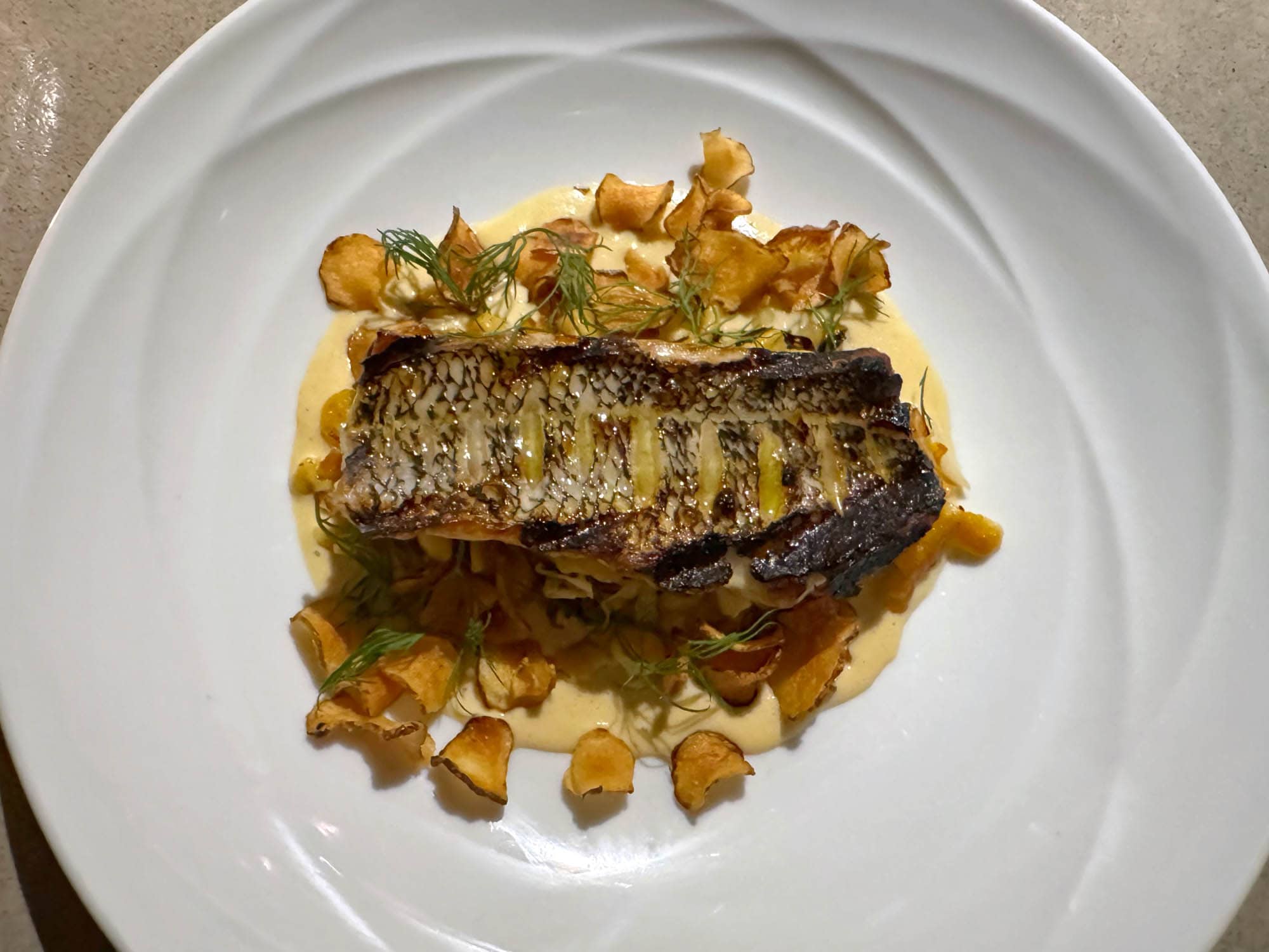 Grilled sea bass filet with sunchoke chips and sauce on a plate.