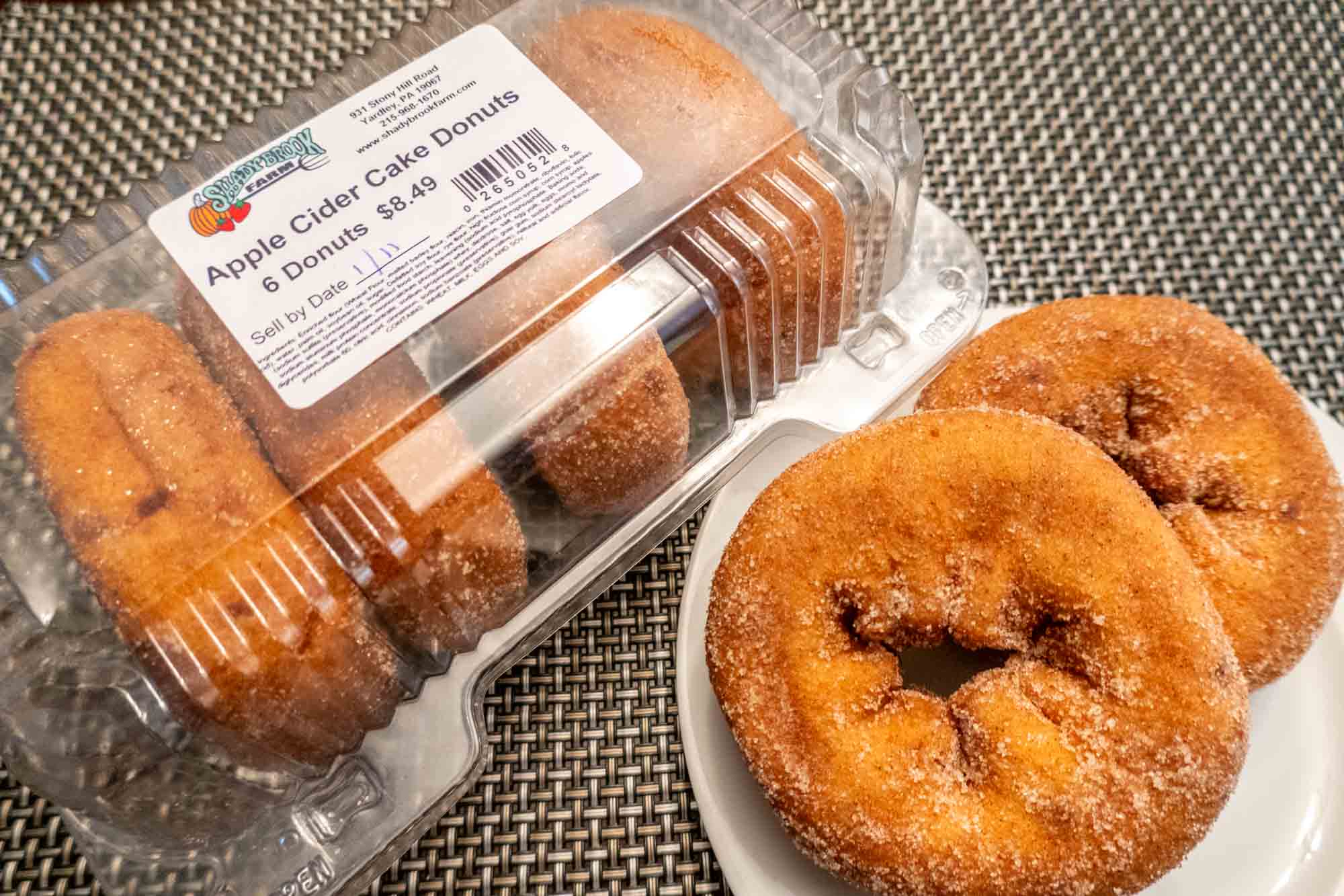 Two donuts on a plate beside a container filled with more donuts