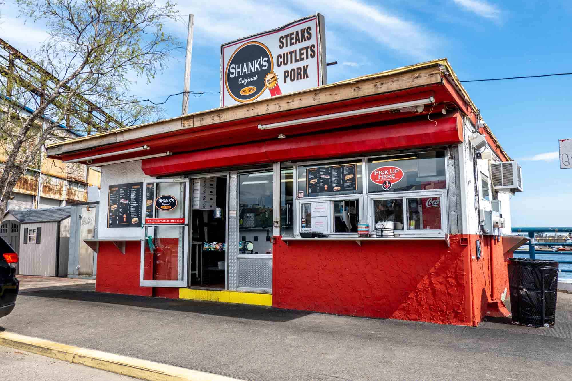 Exterior of a food stand with a pick-up window and sign: "Shank's Original. Steaks, Cutlets, Pork."