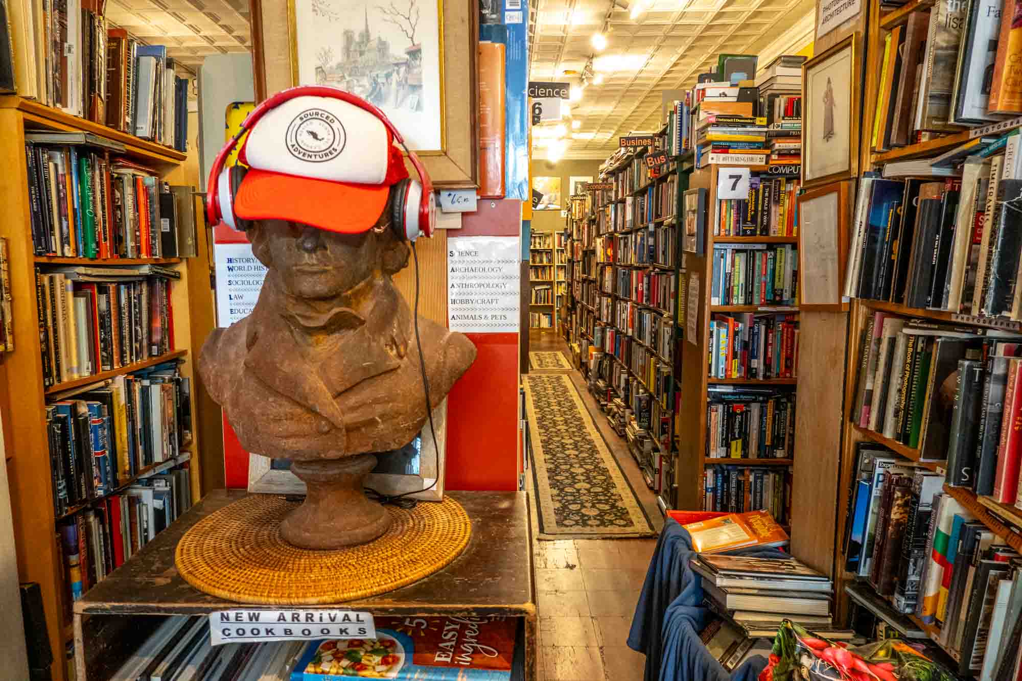 Bookshelves in a used book store with a wooden bust wearing a baseball hat in the foreground.