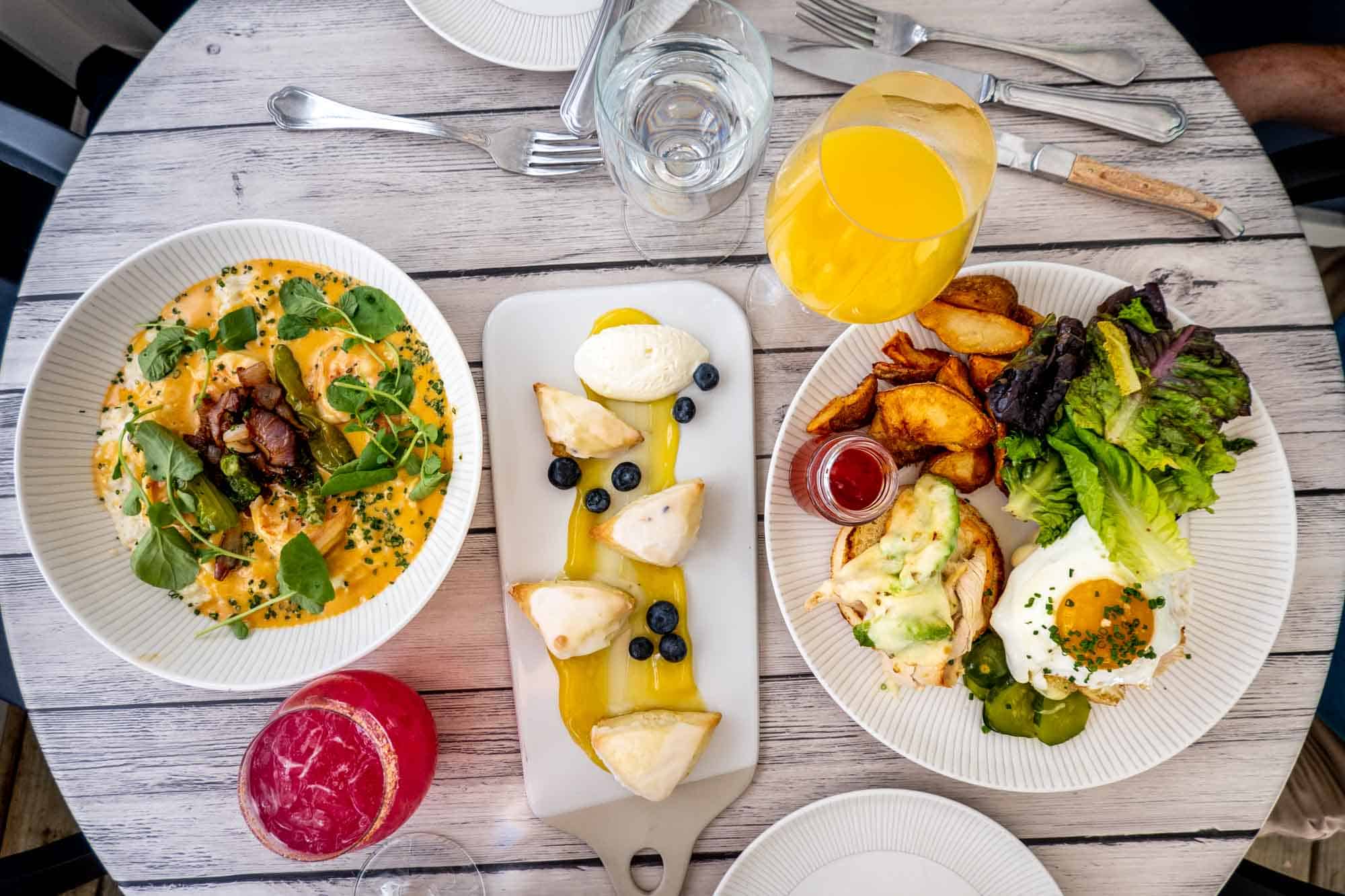 Table with a dish of shrimp and grits, drinks, pastries, and a plate with eggs and potatoes.