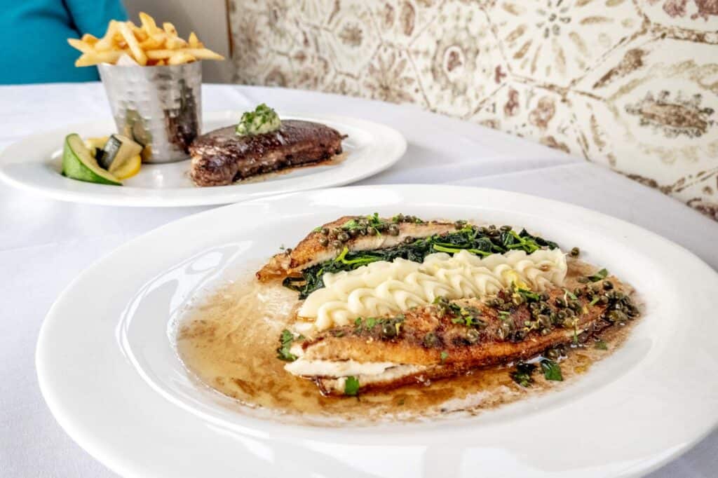 Grilled fish and mashed potatoes on a plate beside a plate with steak and French fries