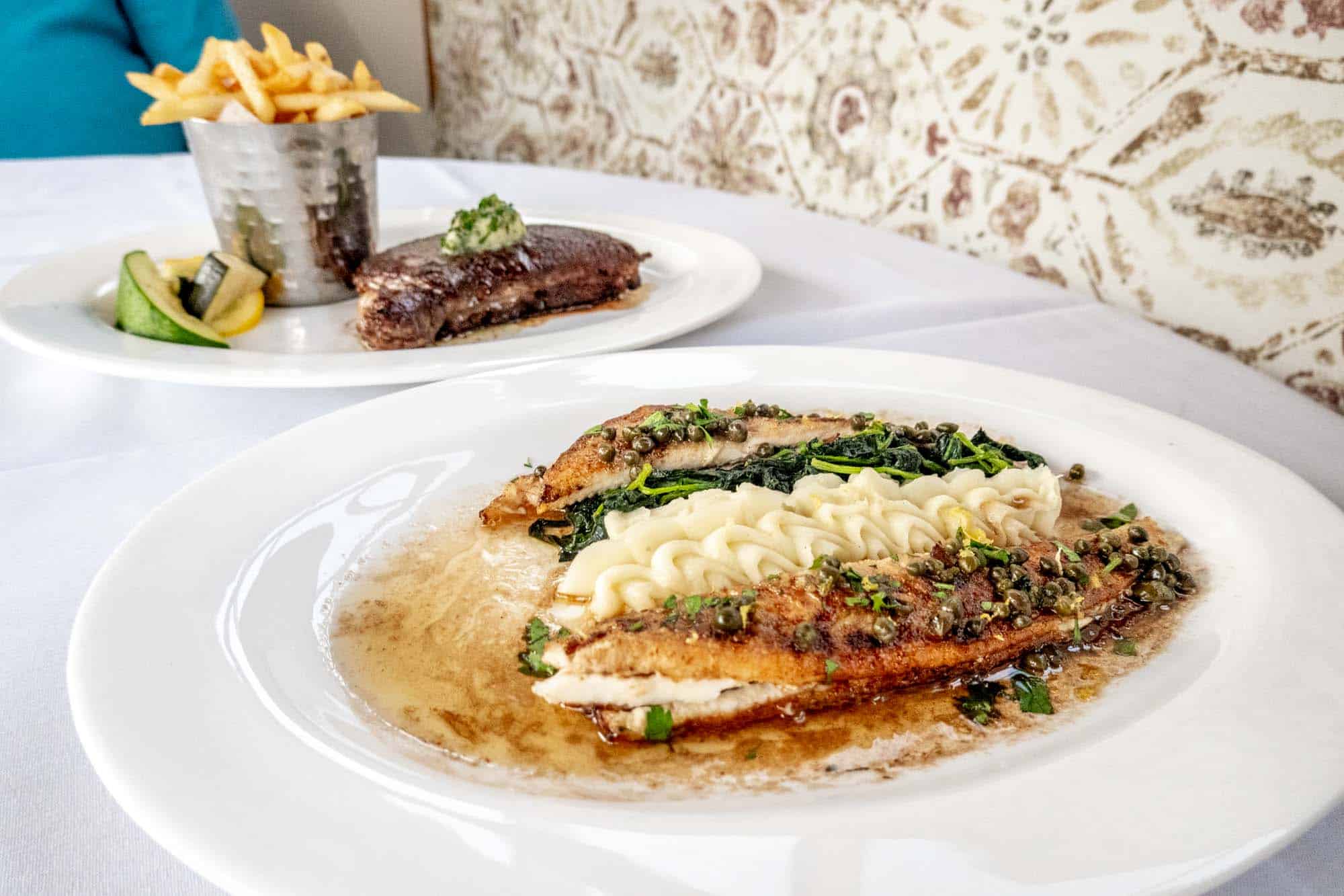 Grilled fish and mashed potatoes on a plate beside a plate with steak and French fries.