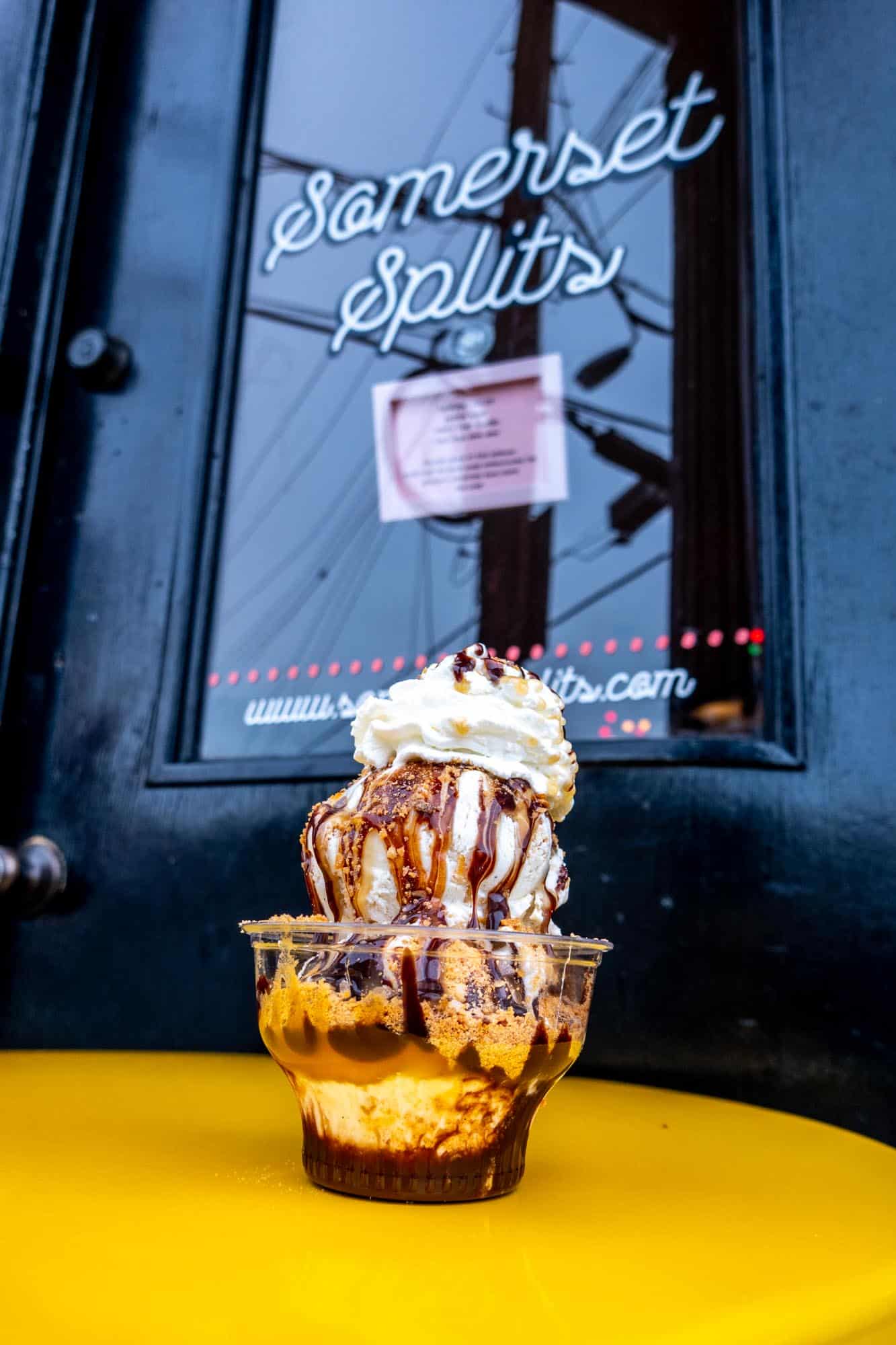 Butterfinger ice cream sundae topped with whipped cream in a cup on a table in front of a door labeled "Somerset Splits"