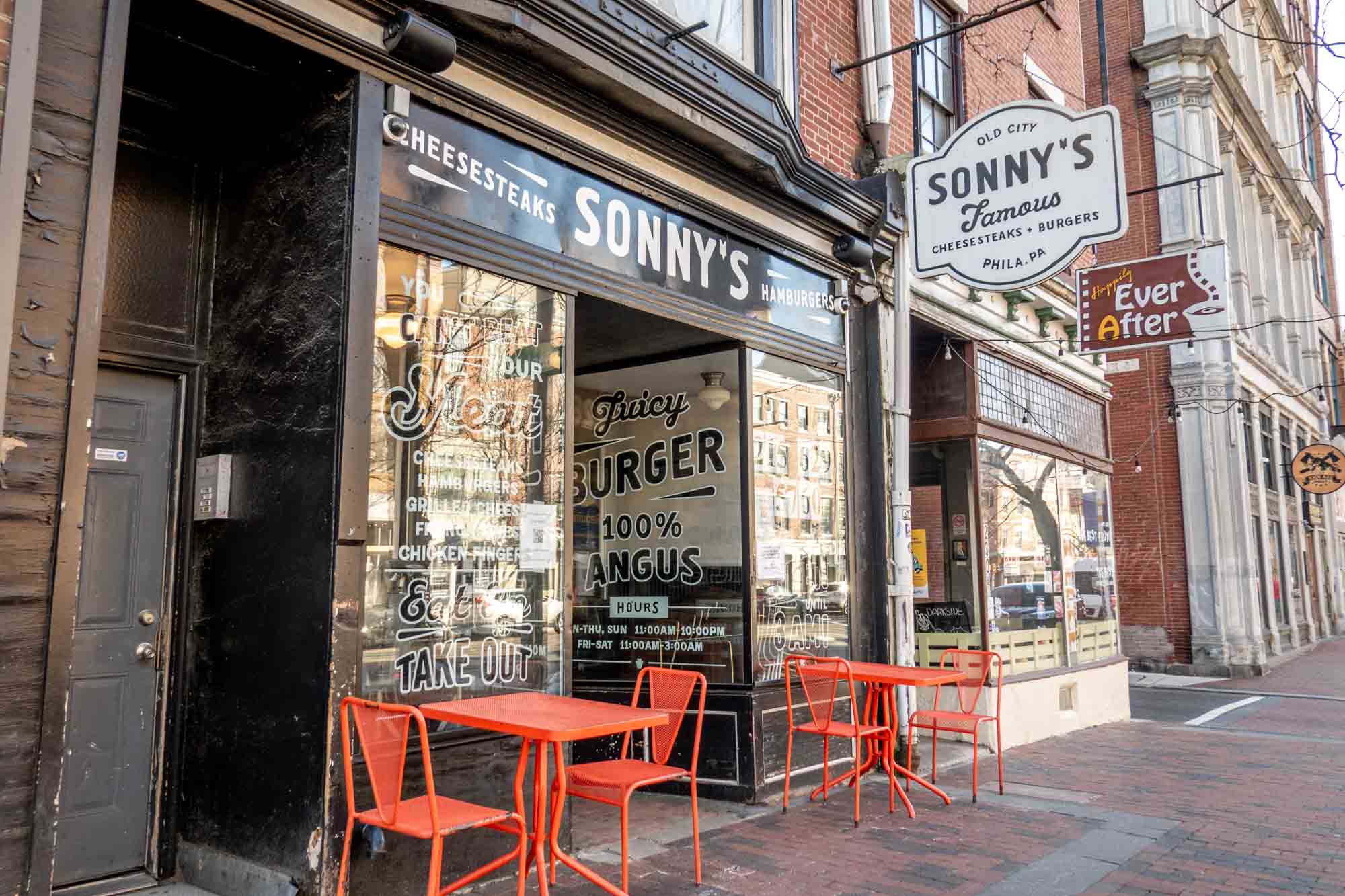 Exterior of a storefront with outdoor tables and a sign: "Old City. Sonny's Famous Cheesesteaks + Burgers. Phila., PA."