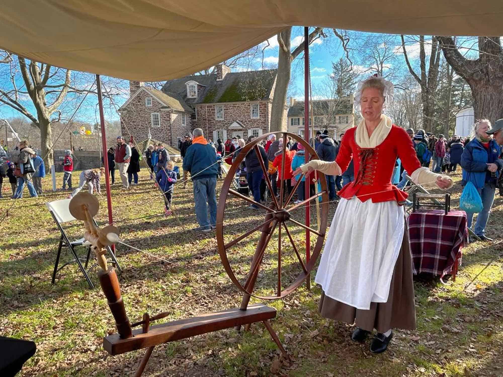 Woman in colonial dress demonstrating a spinning wheel.