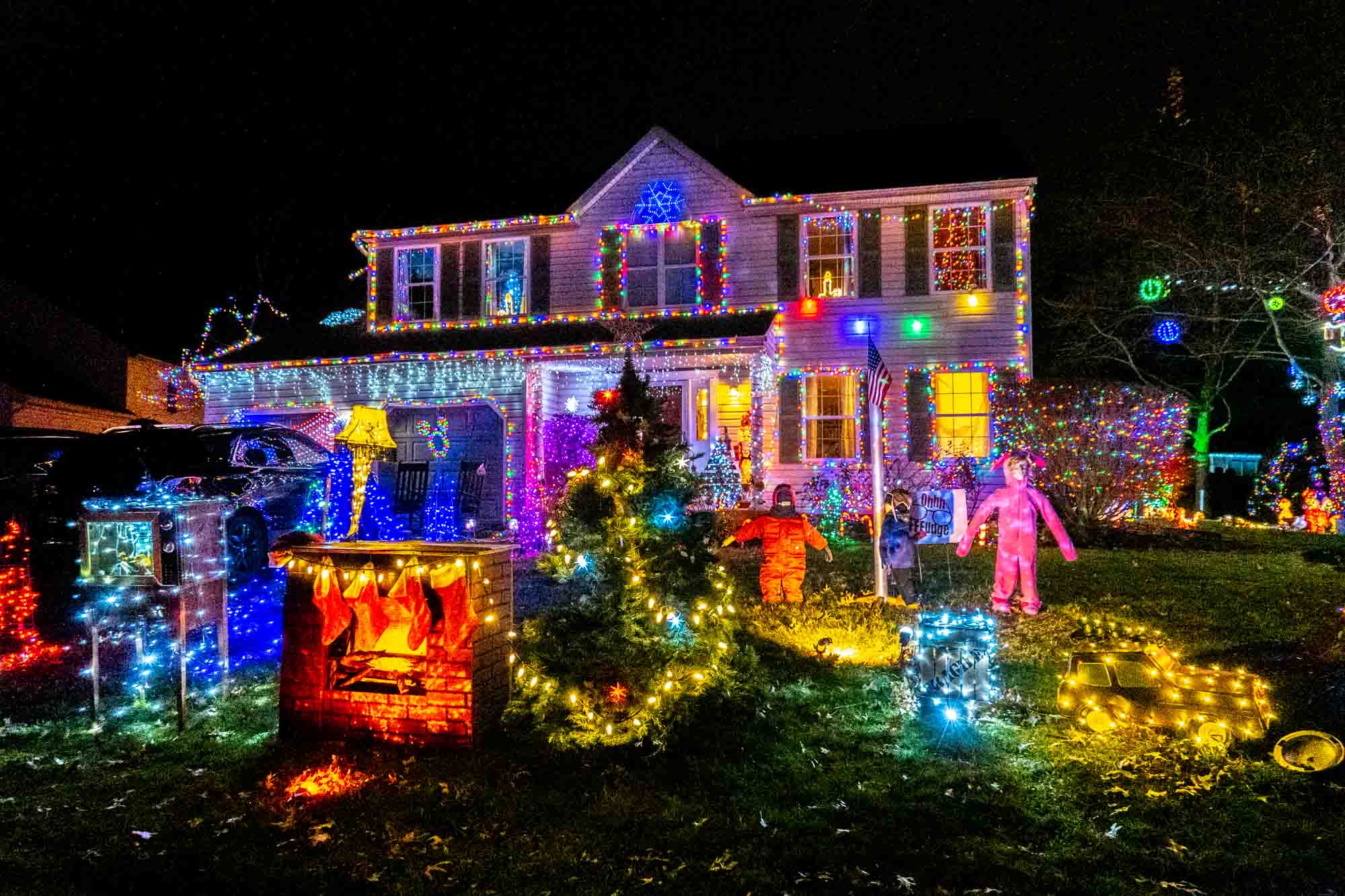 House covered in holiday lights with a Christmas tree, statues, and decorations in the yard.