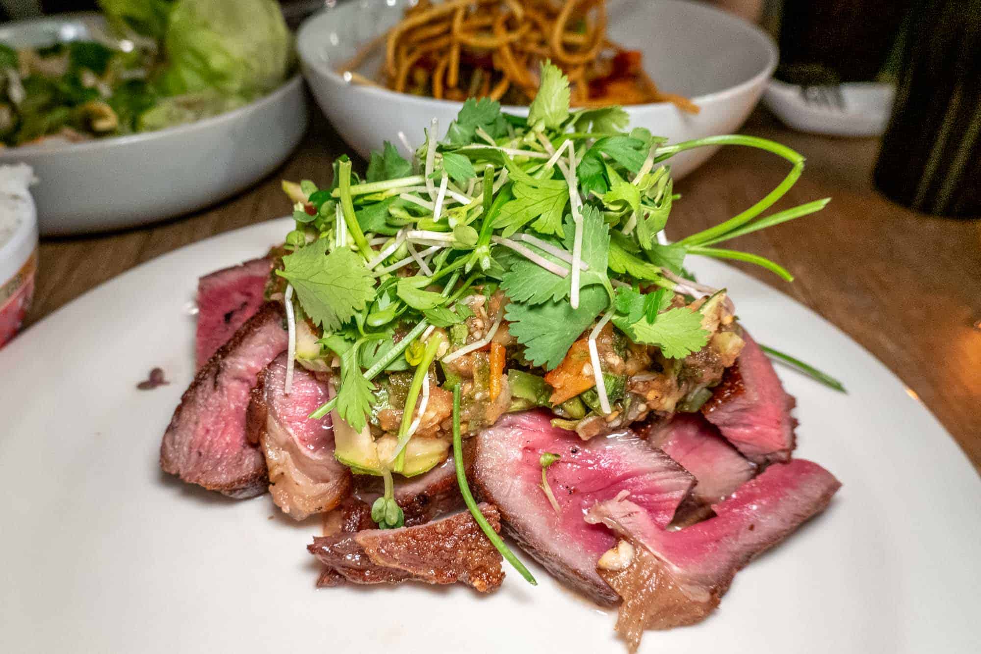 Ribeye steak topped with prohok chutney on white plate