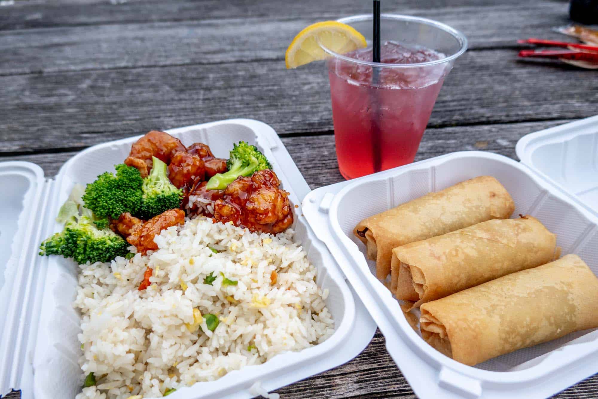 Containers of spring rolls and stir fried chicken and rice on a picnic table