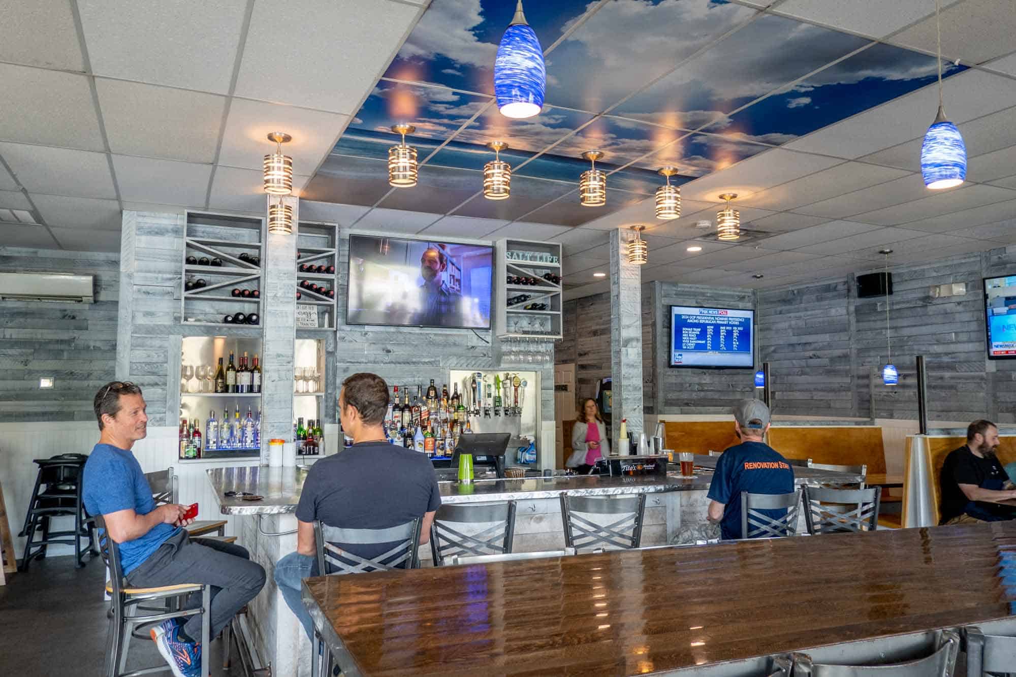 People sitting at a restaurant bar with TVs on the walls