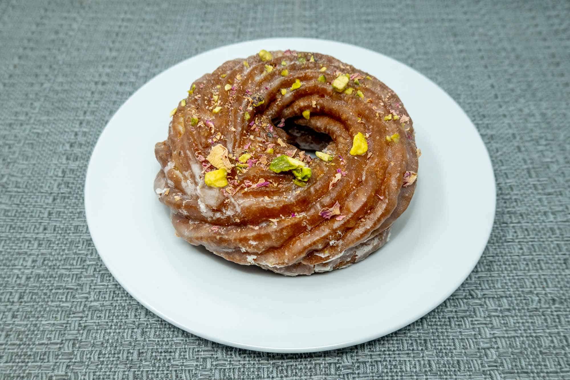 Cruller topped with crushed pistachios on a plate.