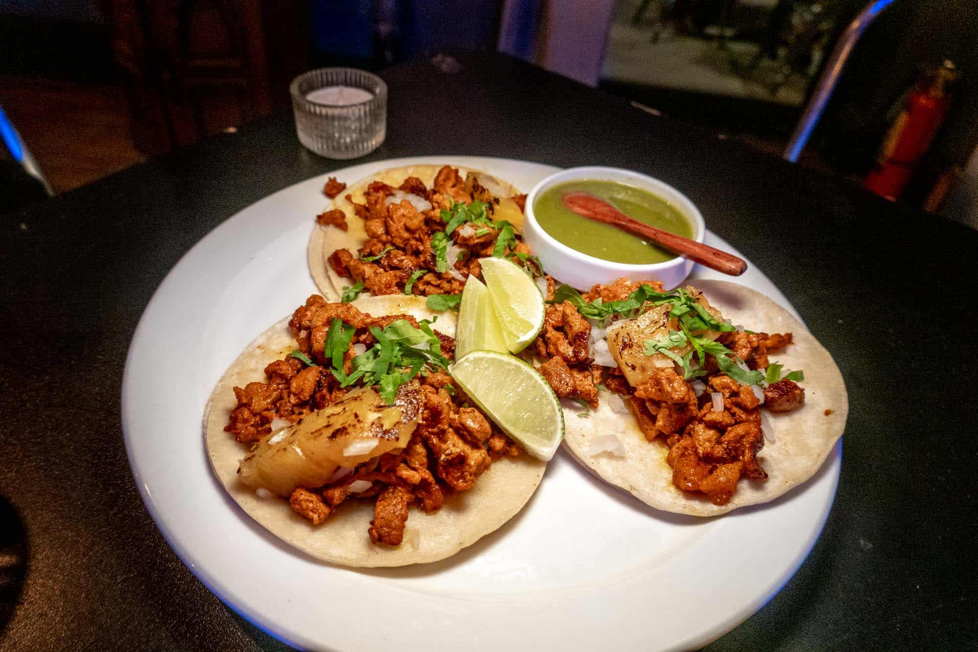 Pork al pastor tacos with lime slices on a plate.