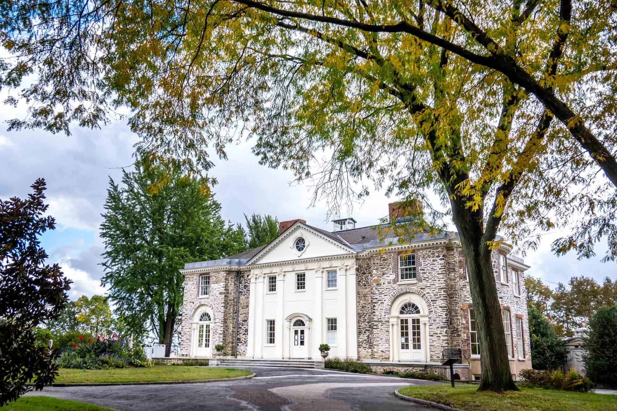 Large stone mansion with arched windows and two chimneys beside a circular driveway.