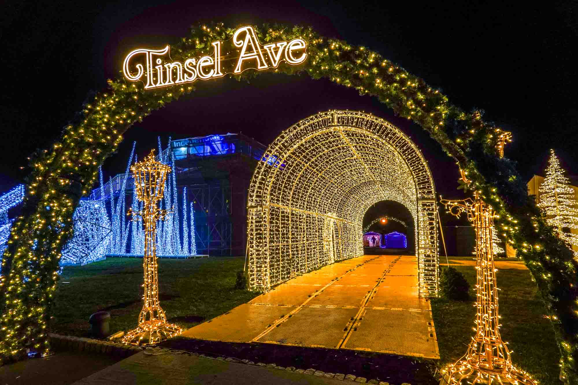 Christmas light tunnel beside a giant garland arch with an illuminated sign for "Tinsel Ave."