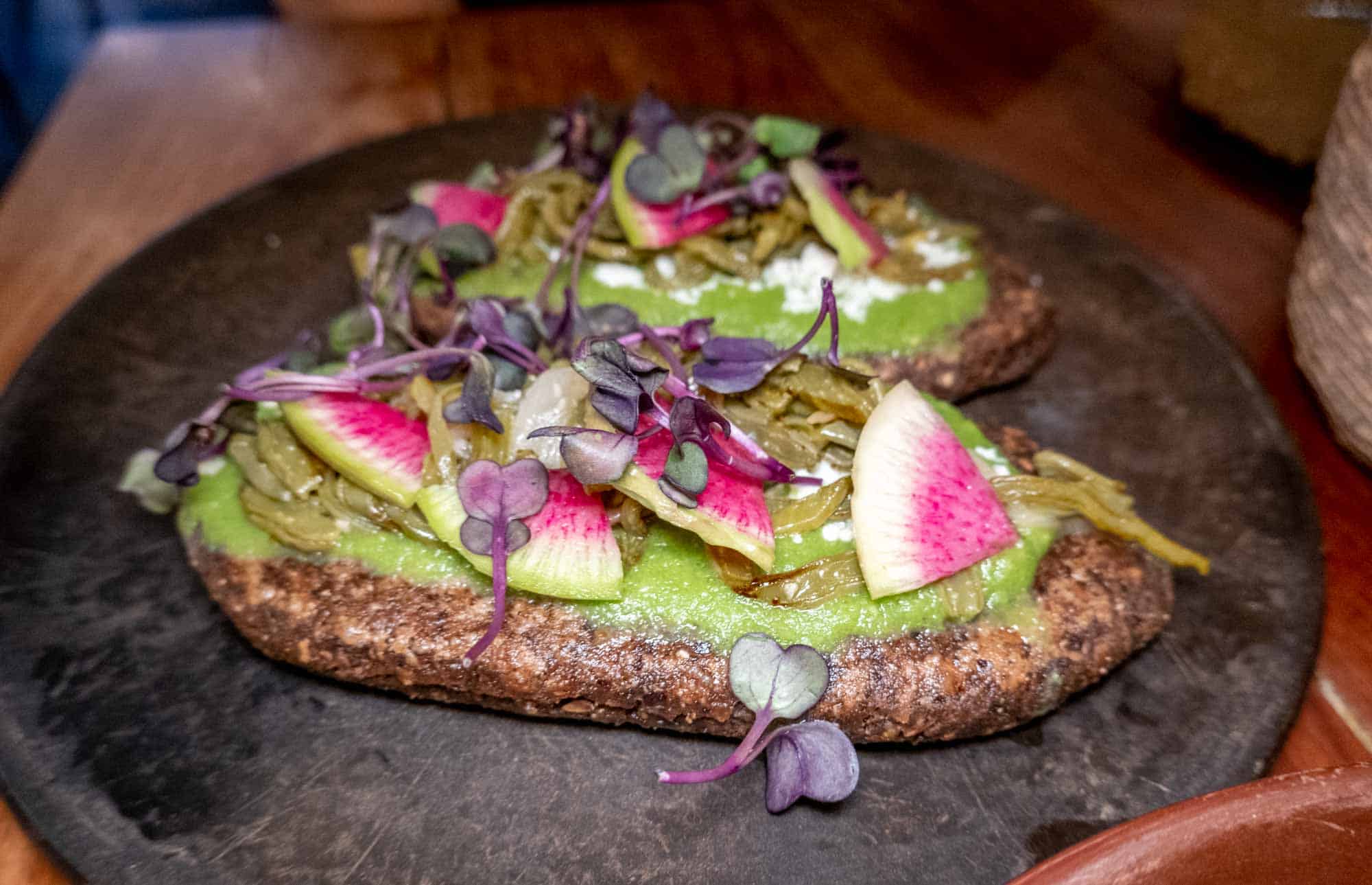 Blue corn masa cakes are stuffed with refried beans, queso fresco, nopales, and then topped with salsa verde and radishes