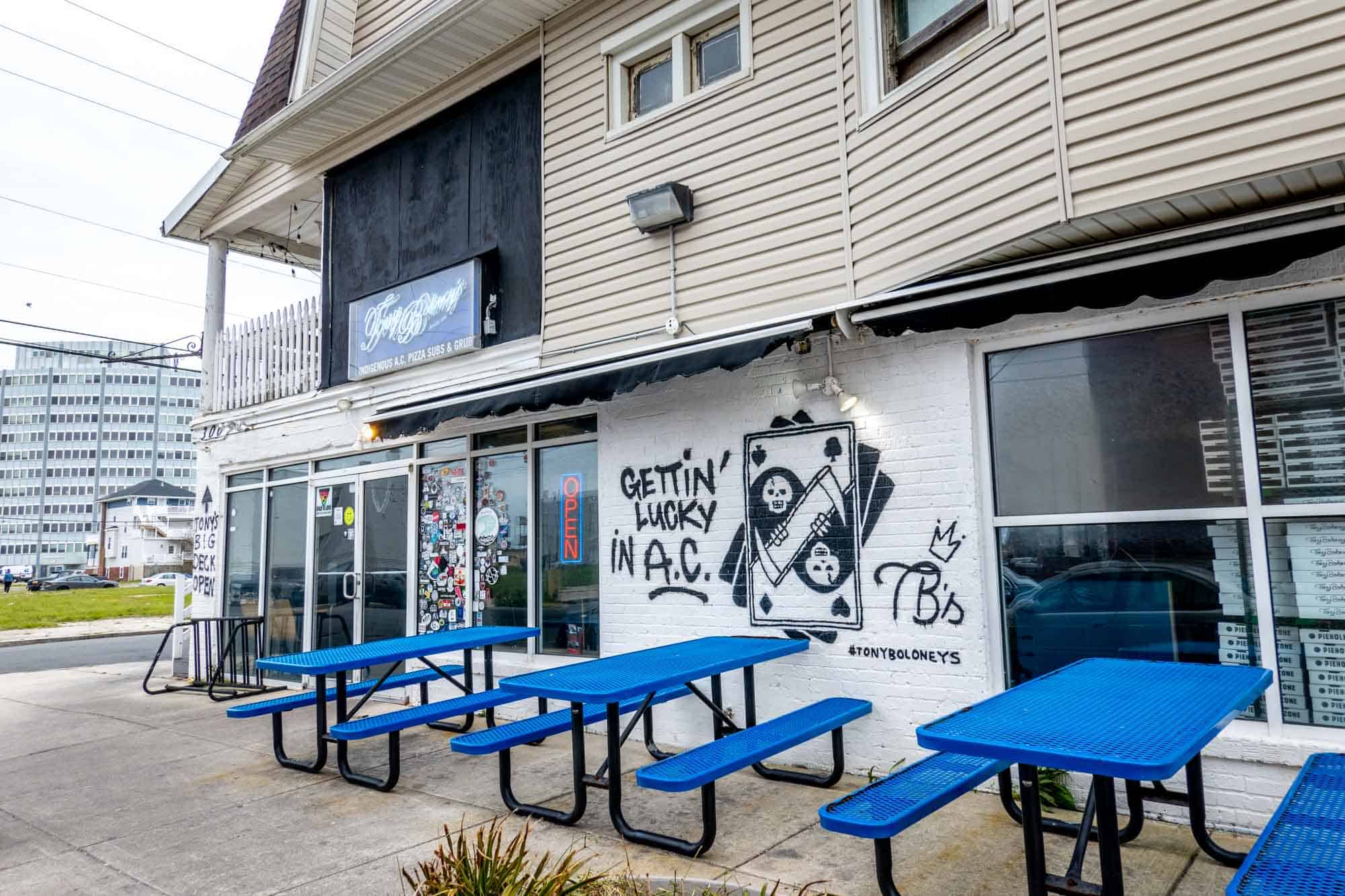 Blue picnic tables outside a white brick building with spray painted artwork on the wall.