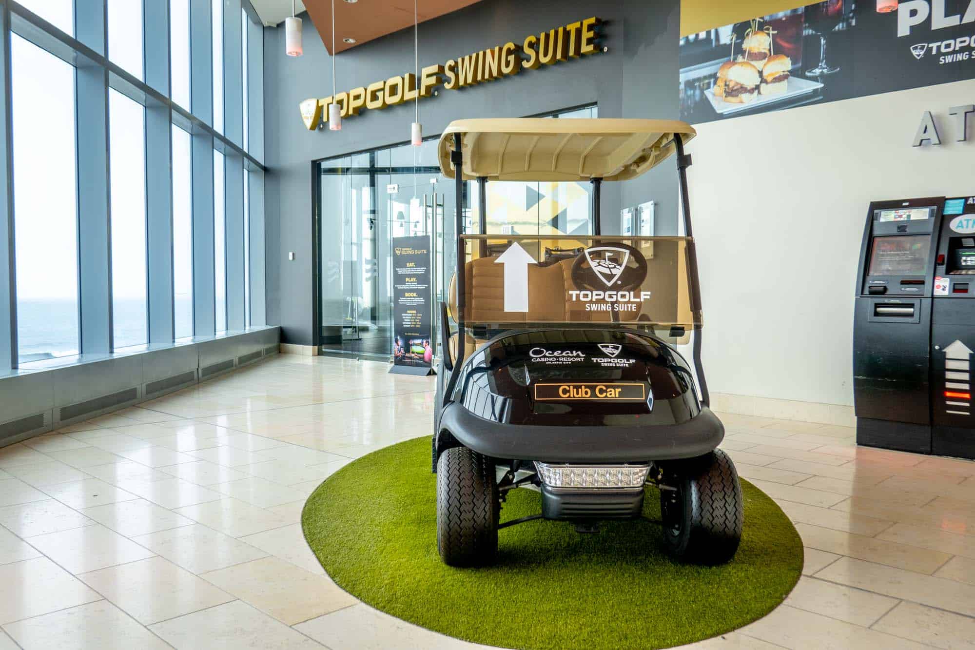 Golf cart indoors, outside of a business with a sign for "Topgolf Swing Suite."