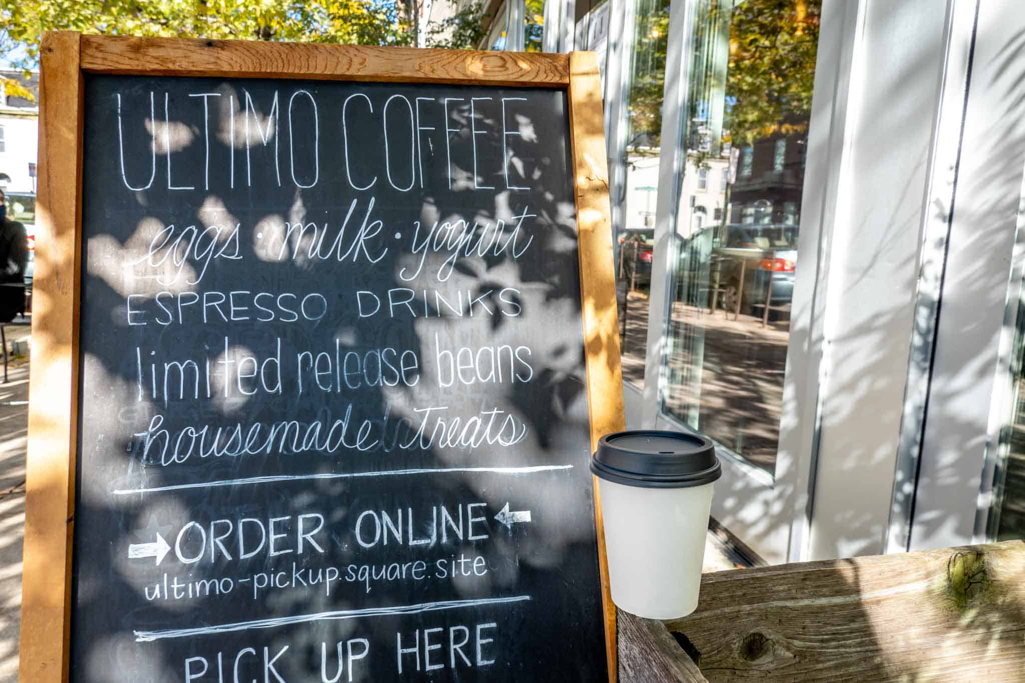 Cup beside a sign: "Ultimo Coffee: eggs, milk, yogurt, espresso drinks, limited release beans, homemade treats."