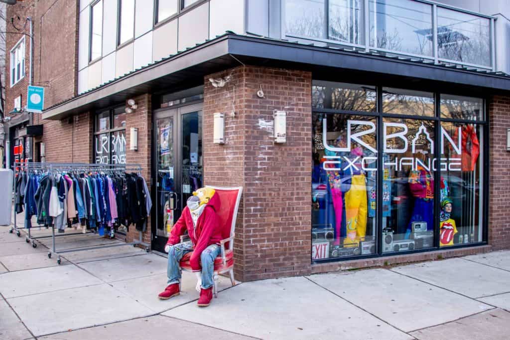 Racks of clothes and a mannequin sitting in a chair outside the brick exterior of a store called Urban Exchange