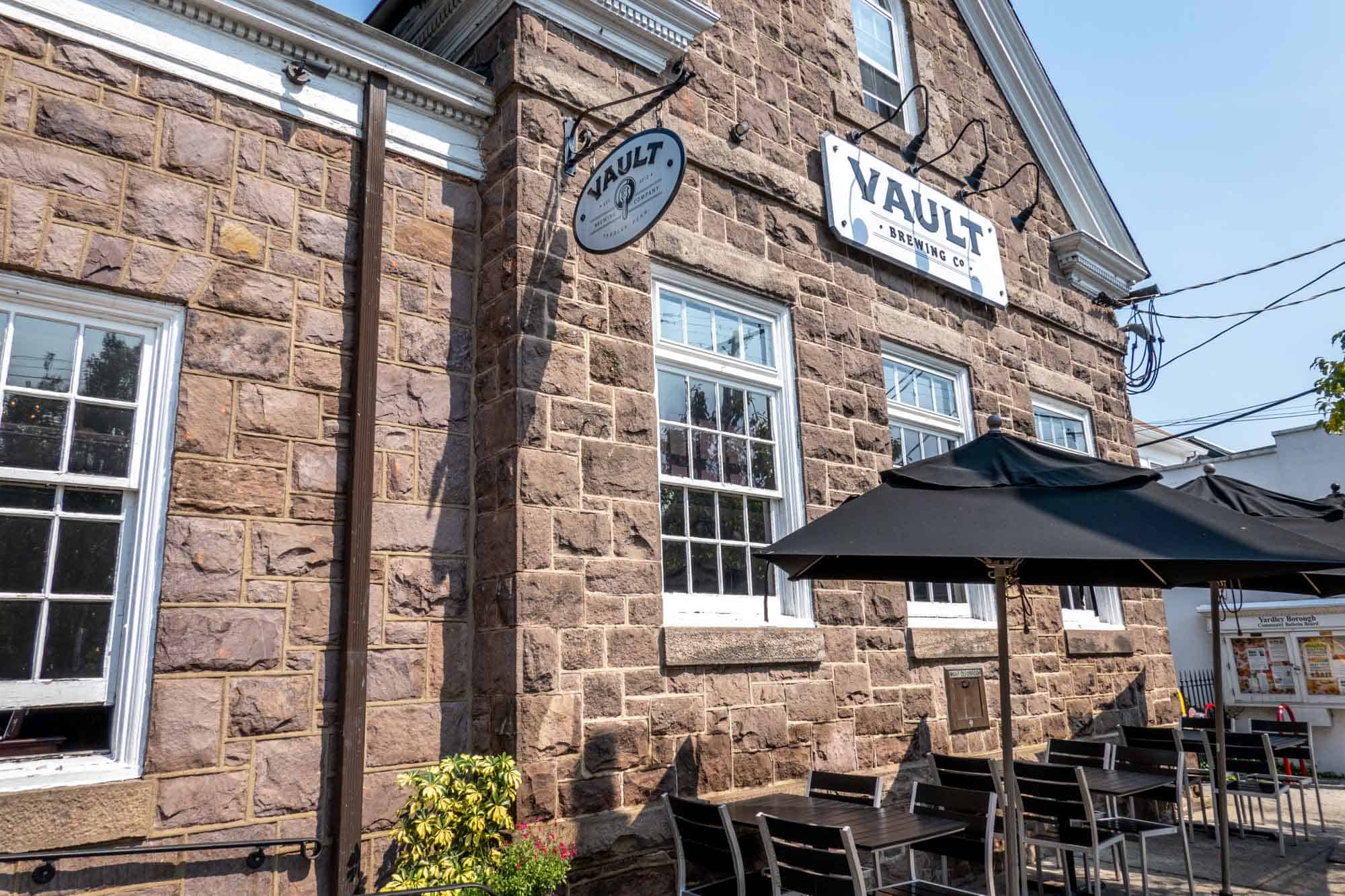 Tables and umbrellas in front of brick building saying Vault Brewing Co