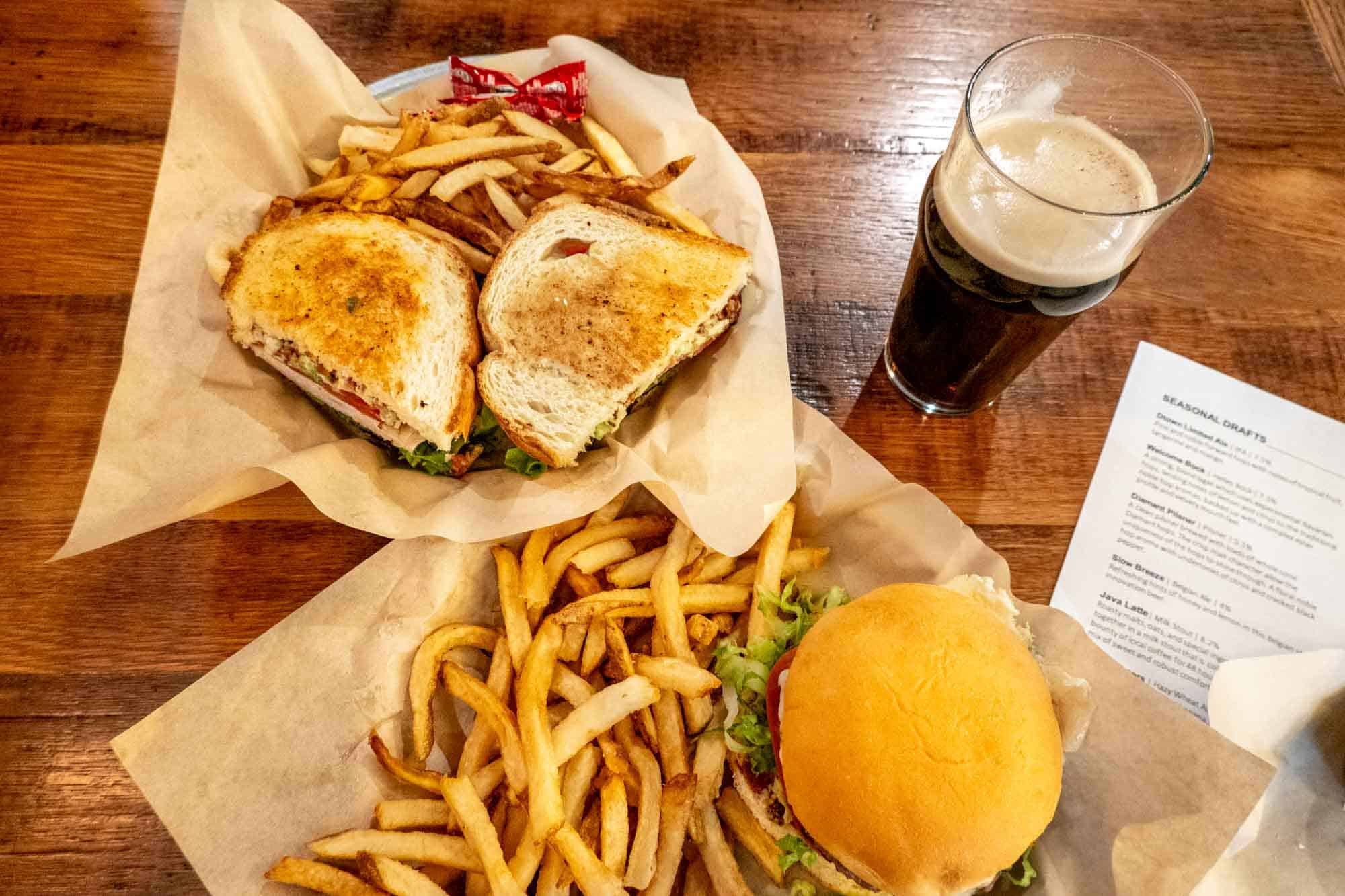 Two sandwiches with french fries and a beer on a table