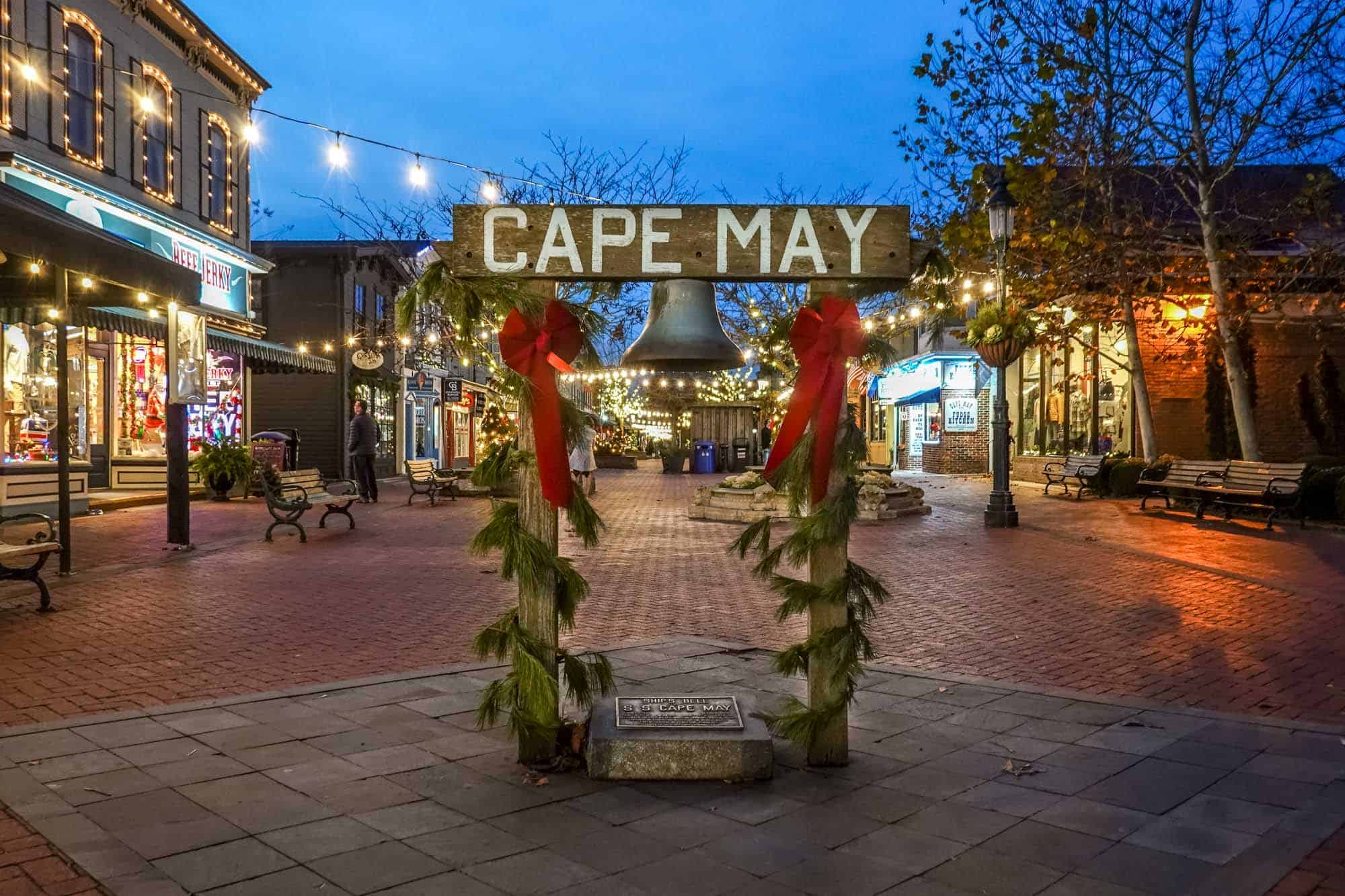 Sign for "Cape May" with a bell hanging from it at a pedestrian shopping mall.