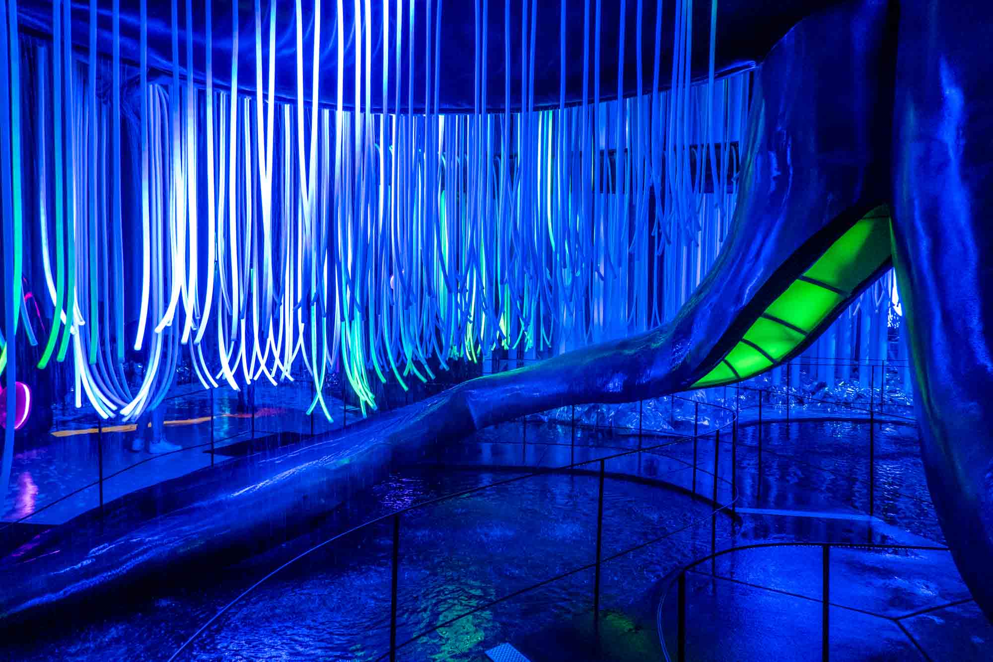 Room with LED lights dangling from the ceiling as water rains down into pools.