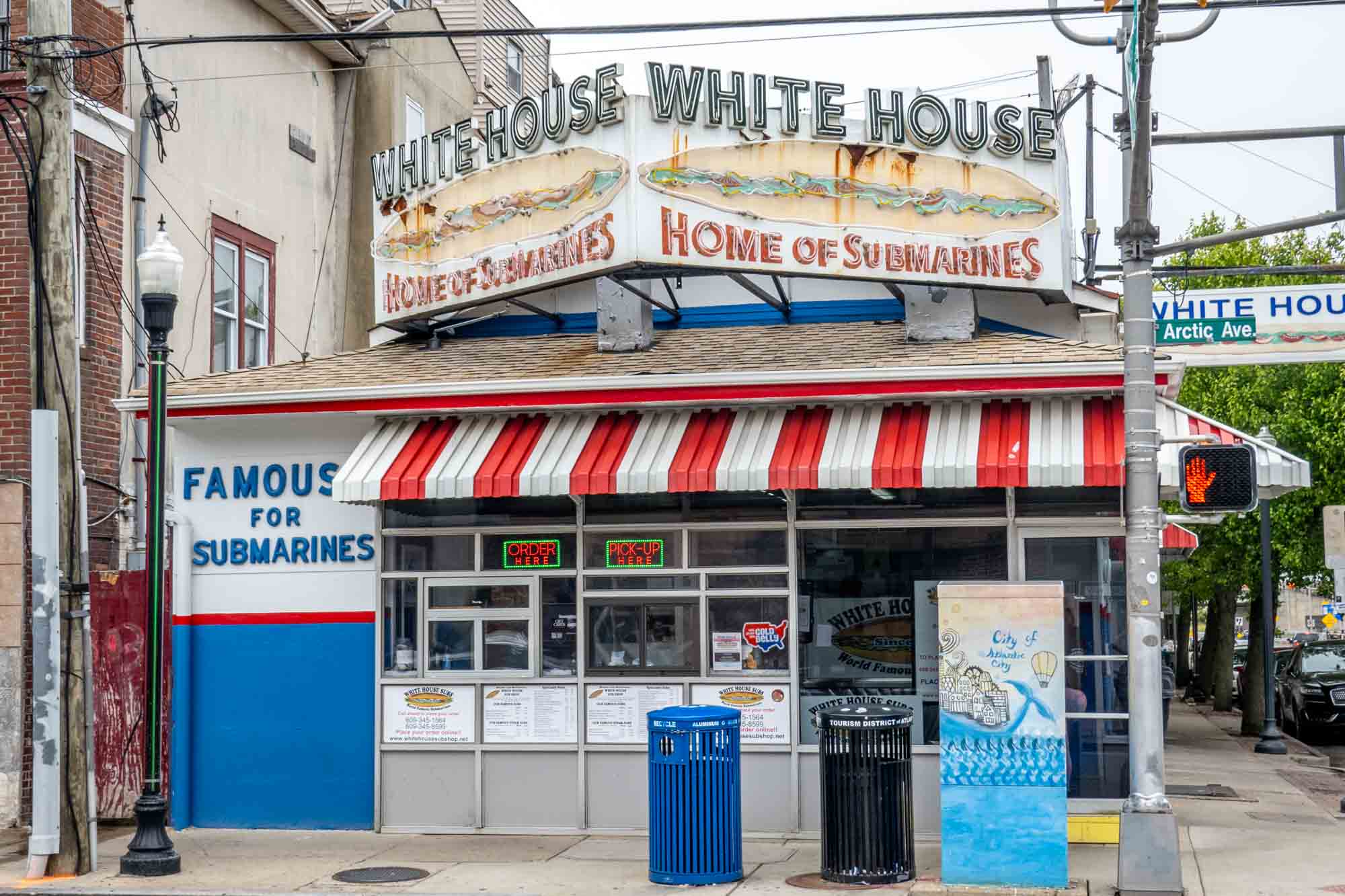 Exterior of a building with a red and white awning and large neon sign for "White House: Home of Submarines."