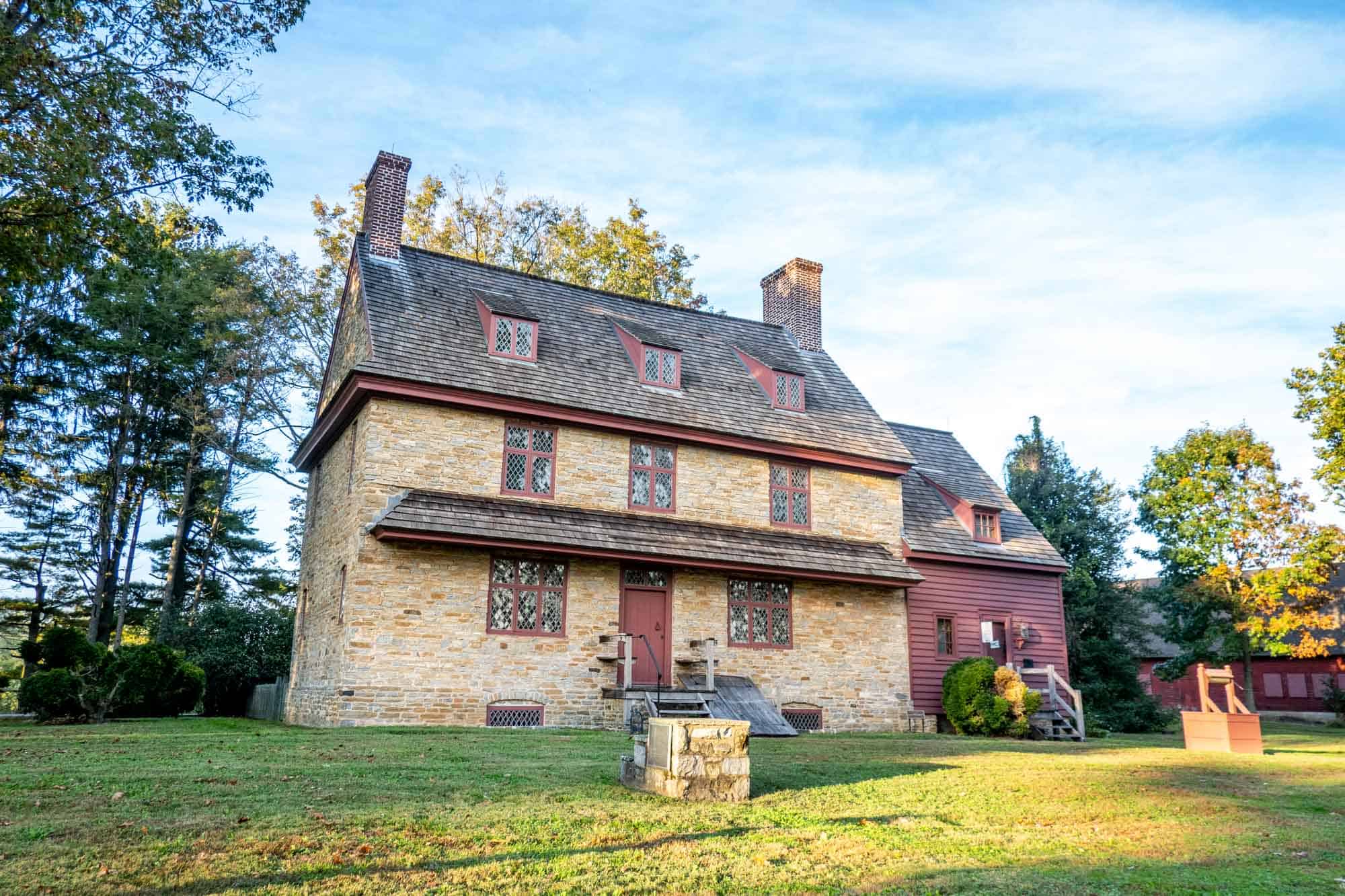 Two-story stone house with two chimneys and two wells in the front yard.