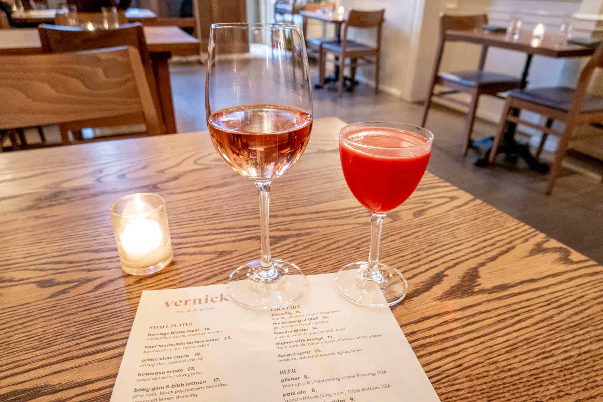 Cocktail and wine glass on a wooden table with a menu for Vernick Food & Drink.